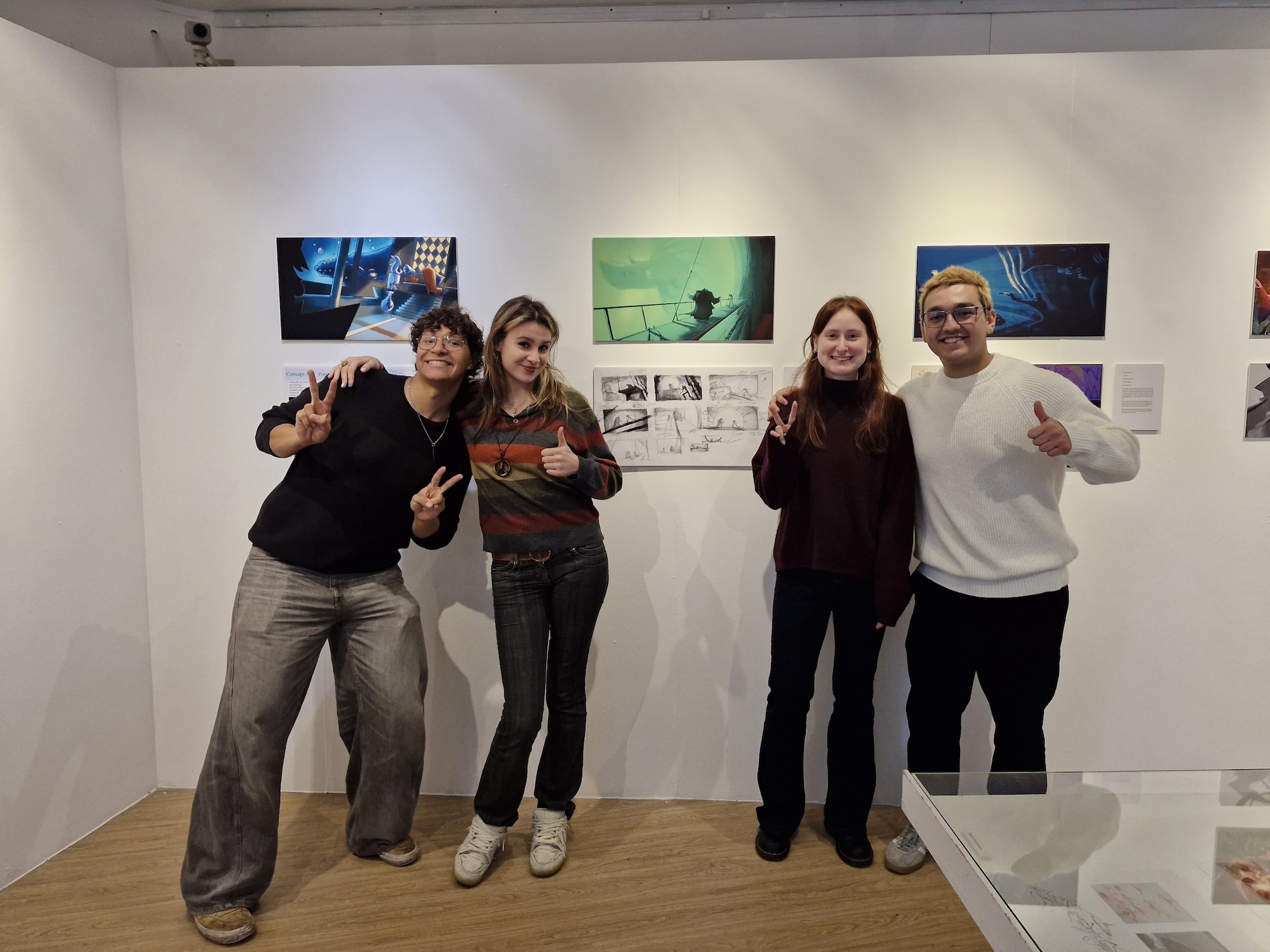 Four BA (Hons) Animation Production students pose next to their concept art, displayed on a wall at the Russell-Cotes Art Gallery and Museum, Bournemouth