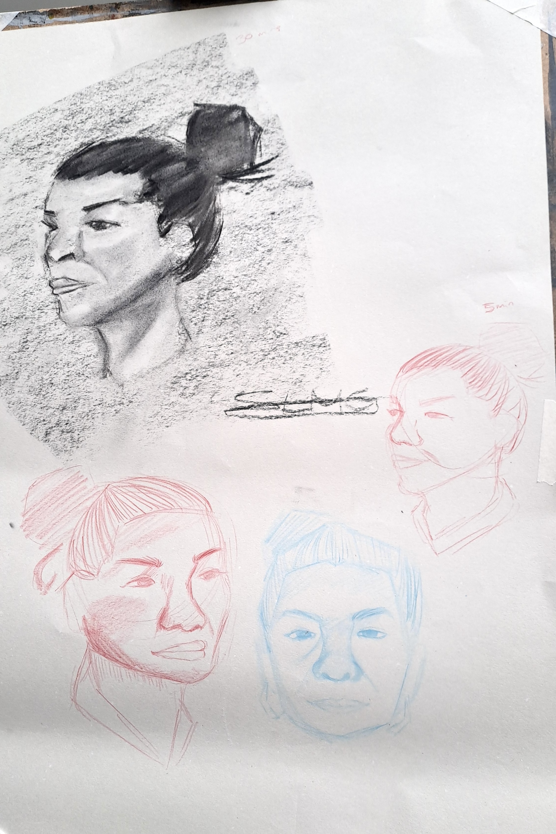 A sheet of paper shows several pencil portrait sketches, including a shaded black-and-white female head in the upper left and three lighter face studies below and to the right.