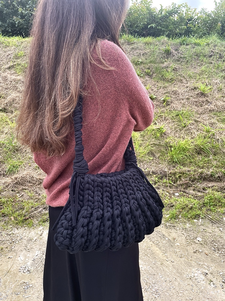 Model wearing a black crocheted bag outdoors.