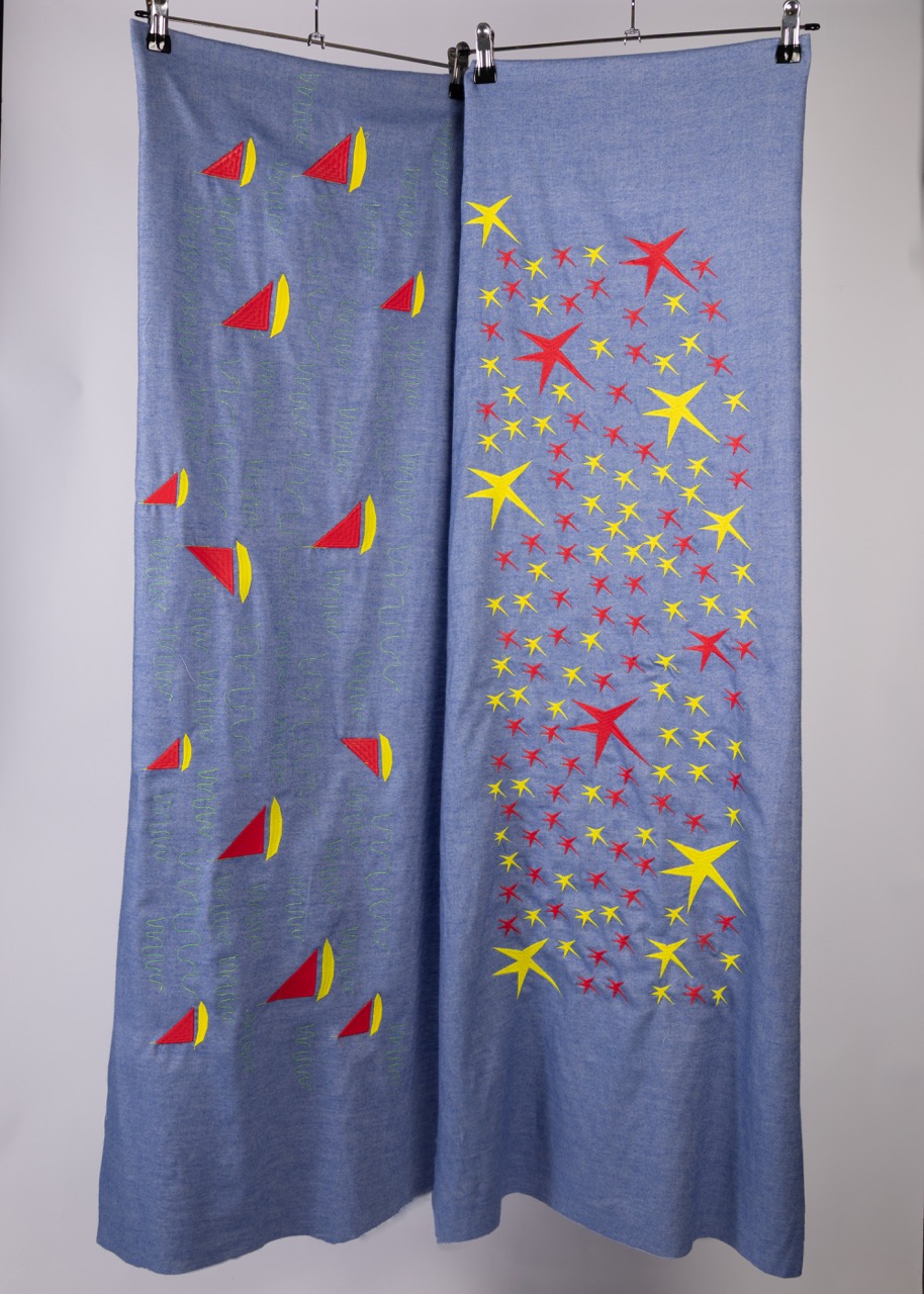 Two fabric panels displayed on hangers, featuring a blue background. The left panel has a pattern of red and yellow sailboat shapes, while the right panel displays a vibrant design of yellow and red stars against the blue fabric.