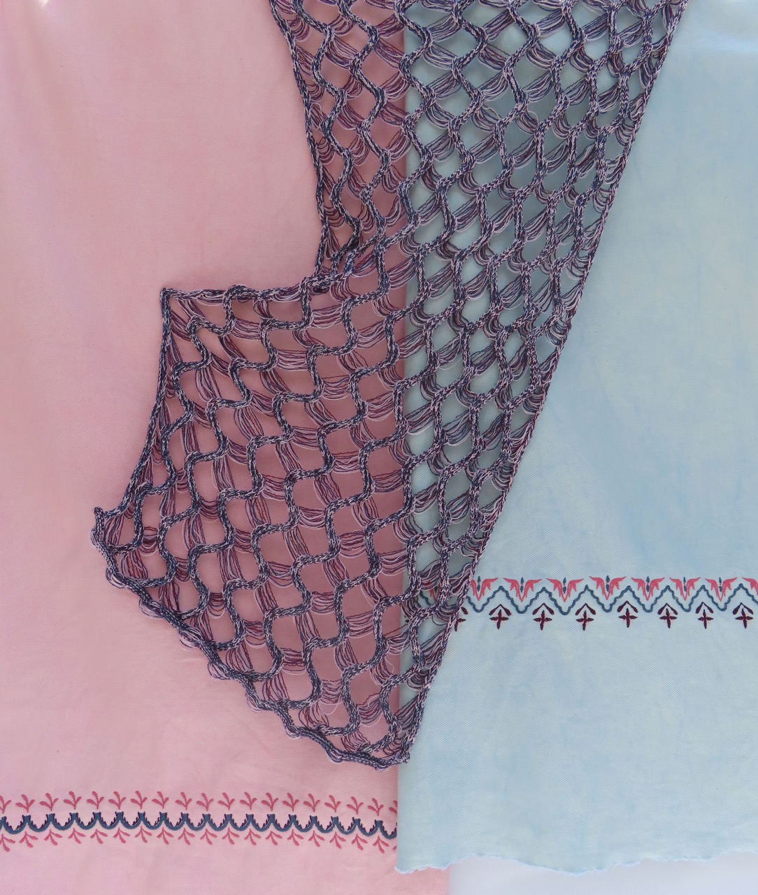 A close-up view of three fabrics arranged together. The left fabric is soft pink with intricate embroidered patterns, the centre fabric features a netted texture in dark blue, and the right fabric is a light blue with decorative stitching along the bottom.