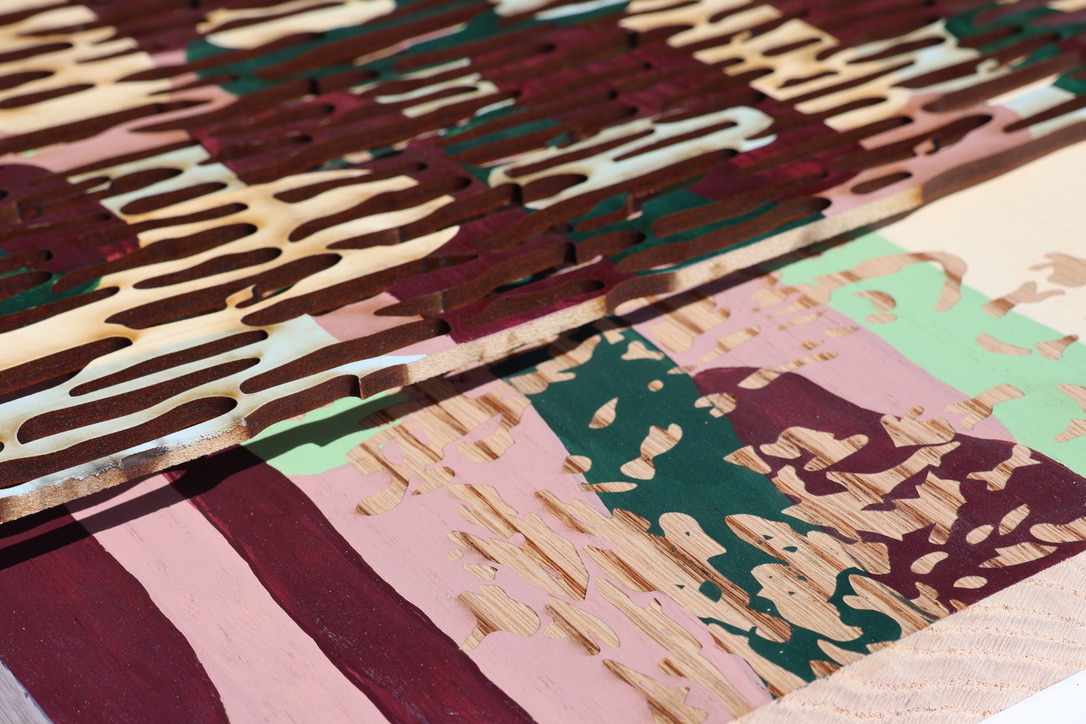 Several layers of wood with different colours and patterns, including shades of burgundy, green, pink, and beige. The textured surfaces show a mixture of smooth and cut-out designs, highlighting the variation in colour and form.