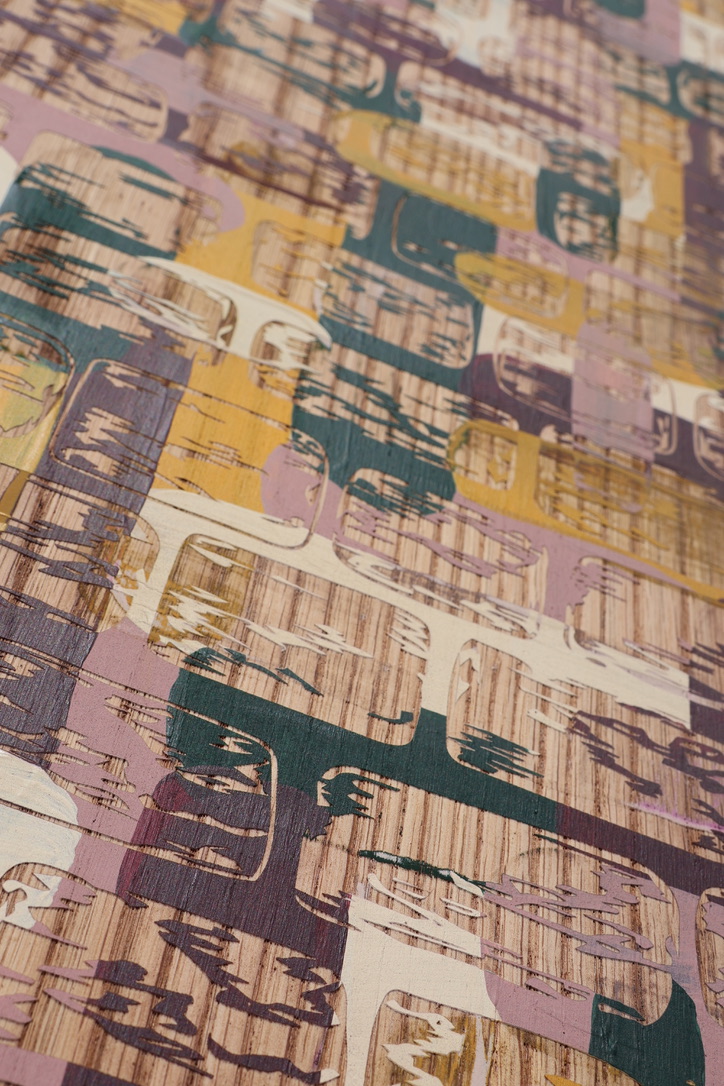 A close-up view of a textured surface featuring an abstract pattern with warm tones of yellow, purple, and green. The design includes overlapping shapes and lines, creating a layered appearance on a light background.