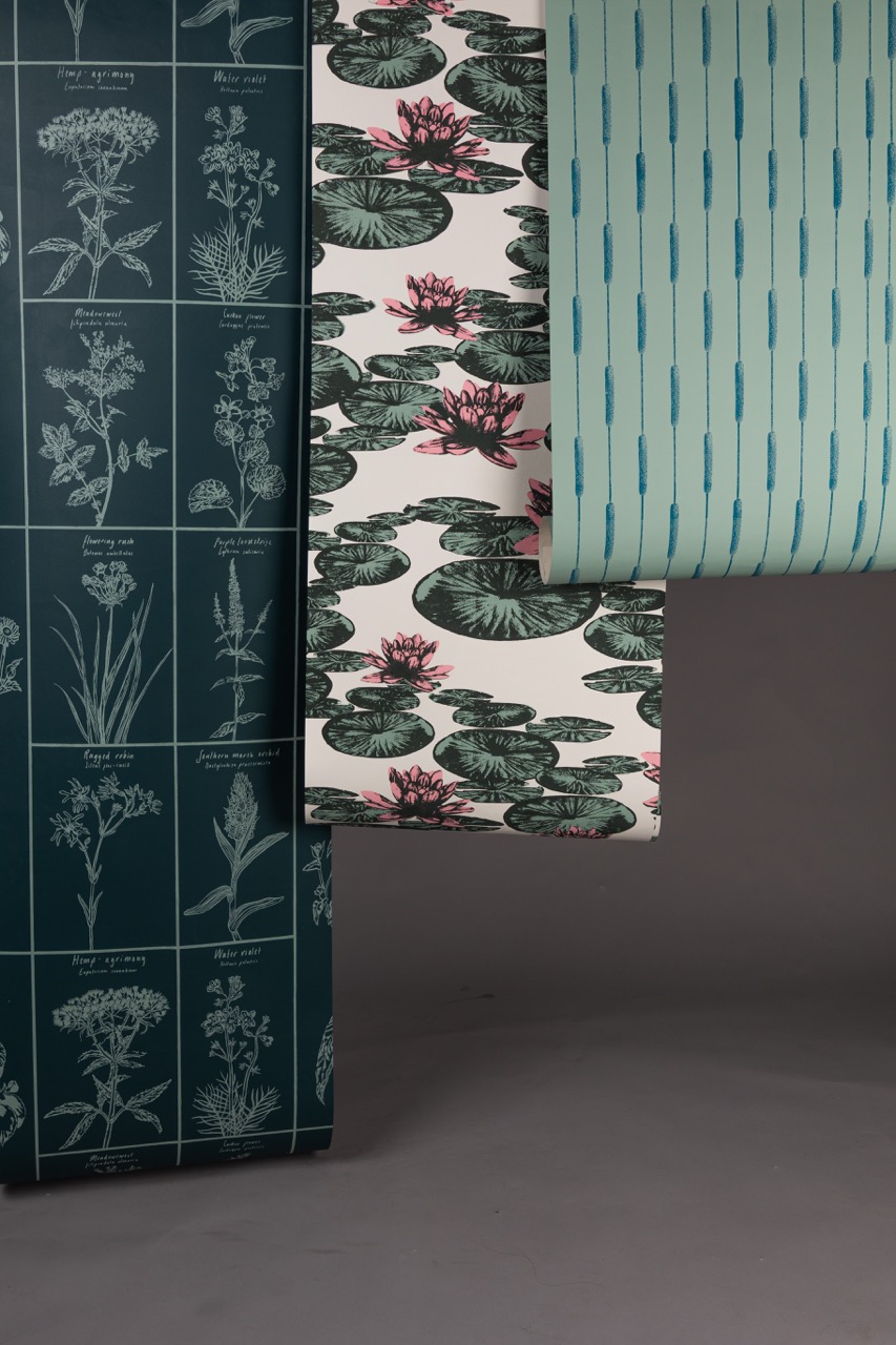 Three different wallpaper samples displayed in a vertical arrangement. The left sample features botanical illustrations on a dark green background, the centre has a floral design with water lilies, and the right presents a light blue pattern with thin vertical lines.