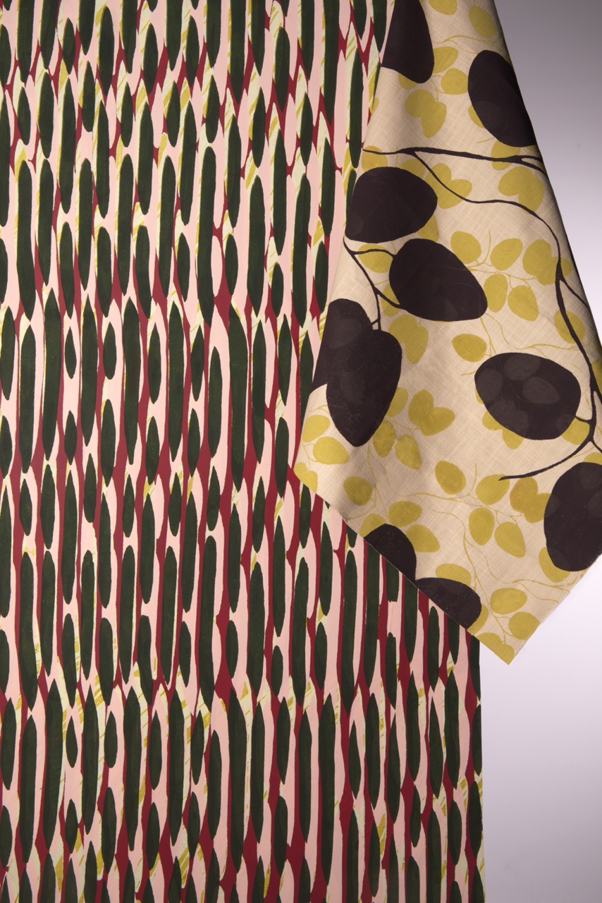 A close-up of two fabric samples featuring distinct patterns. The left sample has vertical green and red stripes on a beige background, while the right sample showcases branches with black leaves and yellow hearts against a cream background.