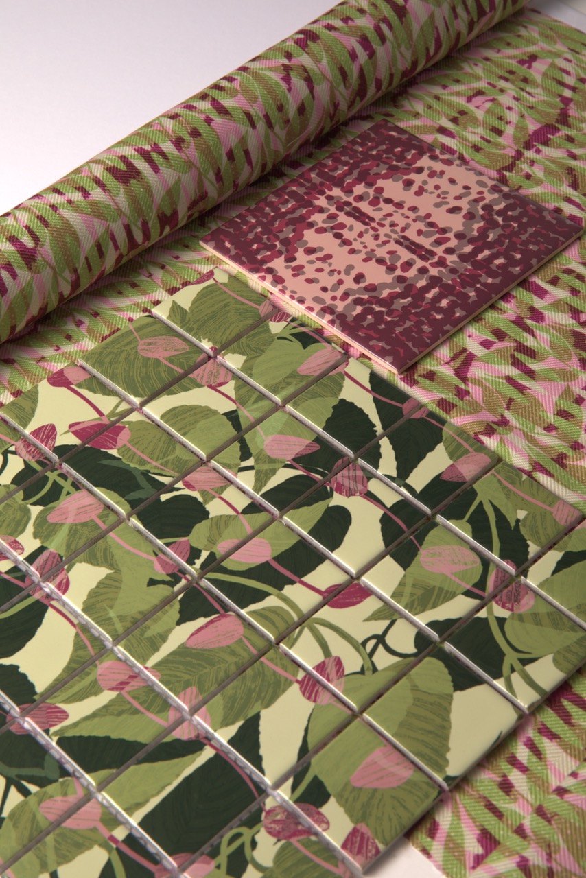 A sample of patterned tiles with a floral design featuring green leaves and pink buds is laid out. Above, a rolled fabric with a coordinating print displays abstract shapes in shades of pink and green.