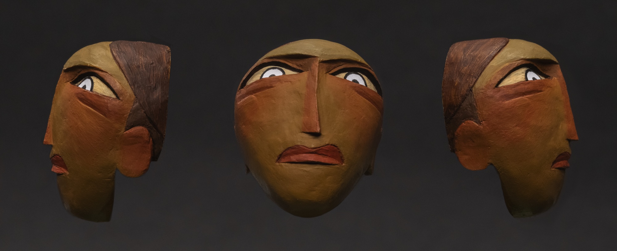 Detailed painted sculpture of face with serious expression, wide eyes and thin, long nose, left, front and right view. Dark background.