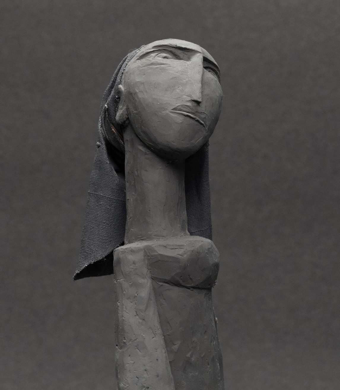 Dark sculpture of a person's head and neck, posed upright in a serious expression, thin eyes and long, thin nose.