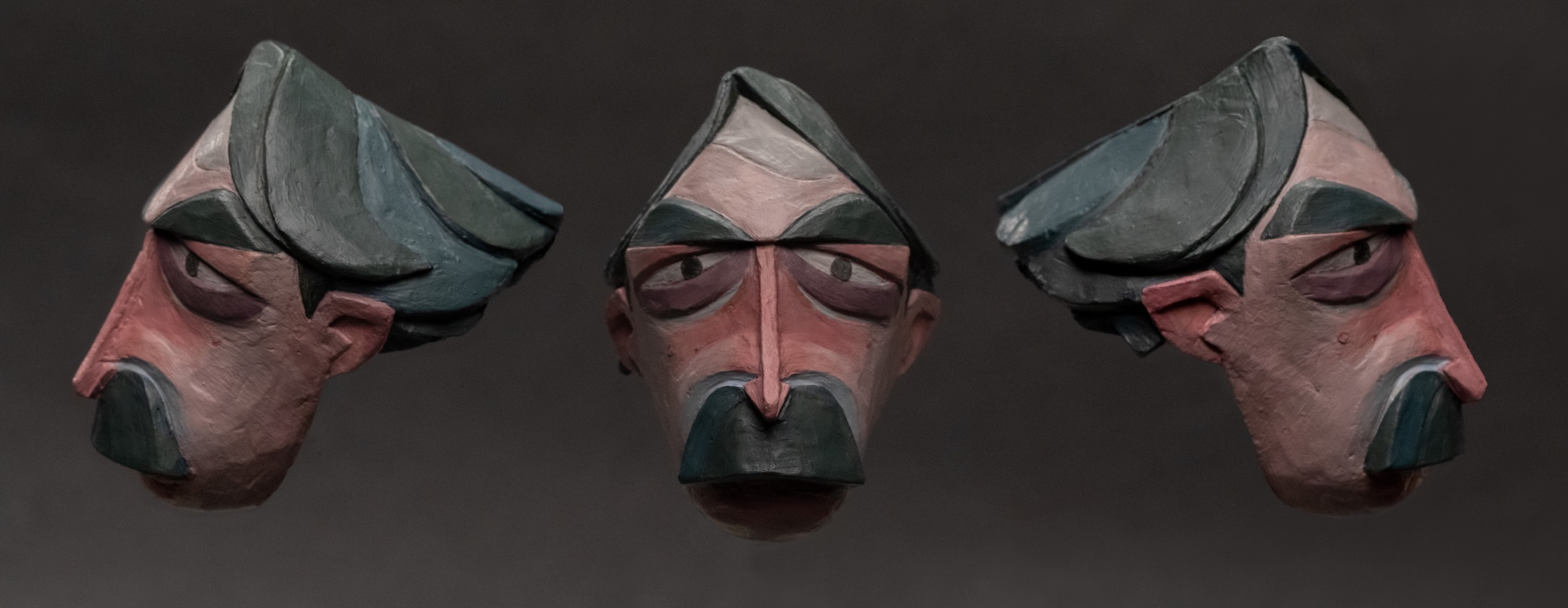 Detailed wooden sculpt of a serious character with red blush, grey hair and facial hair, left, front and right sides, dark background.