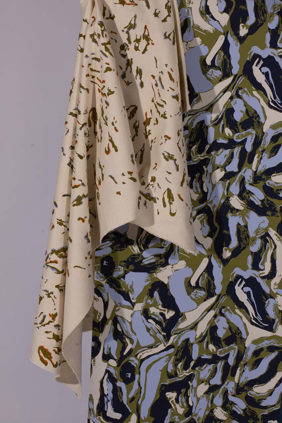 A piece of fabric draped over a patterned garment. The main fabric features organic shapes in shades of blue, green, and beige, while the draped fabric is a solid beige with a subtle texture.