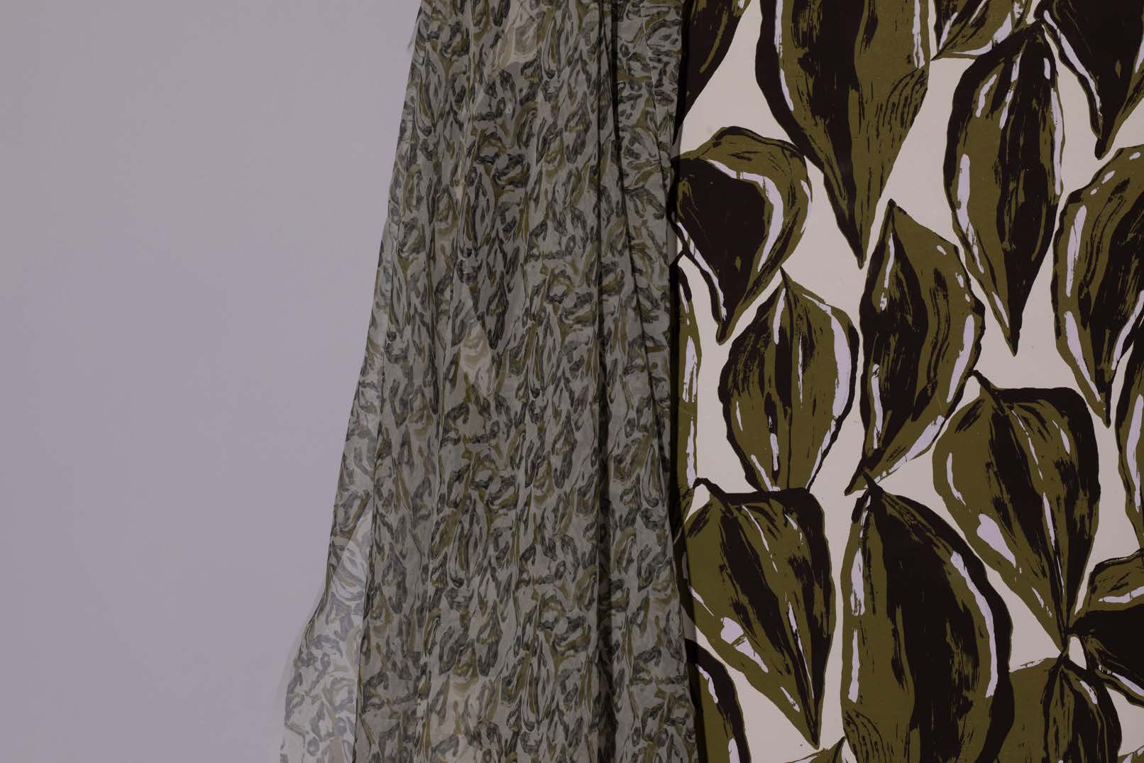 Two pieces of fabric displayed together. The first is a sheer grey fabric with a subtle floral pattern, while the second is a thicker fabric featuring a bold green and cream botanical design.