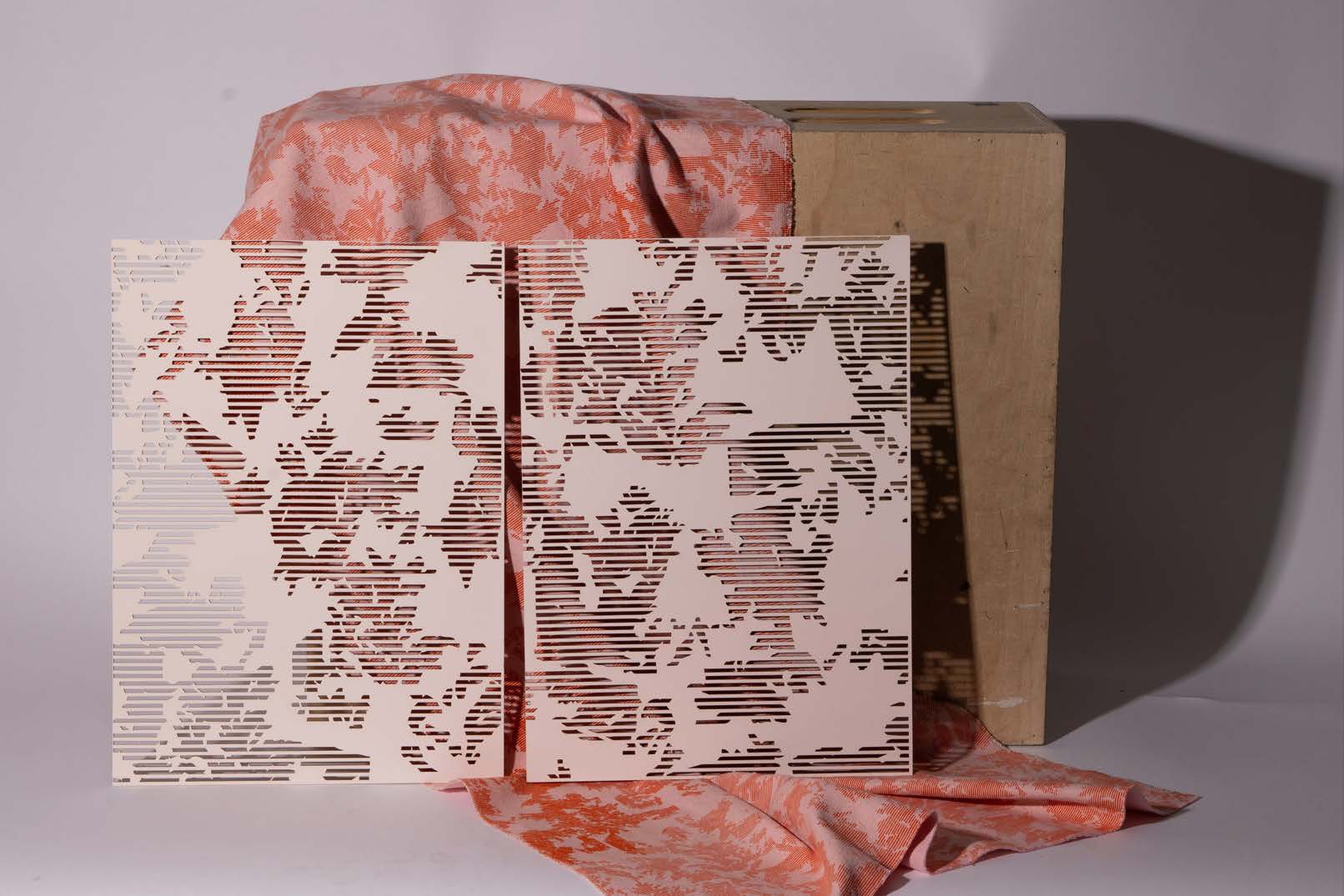 Two laser-cut panels with a floral pattern layered over a textured fabric in shades of peach, draped over a beige box. The panels exhibit a combination of solid and open spaces, creating a modern design effect.