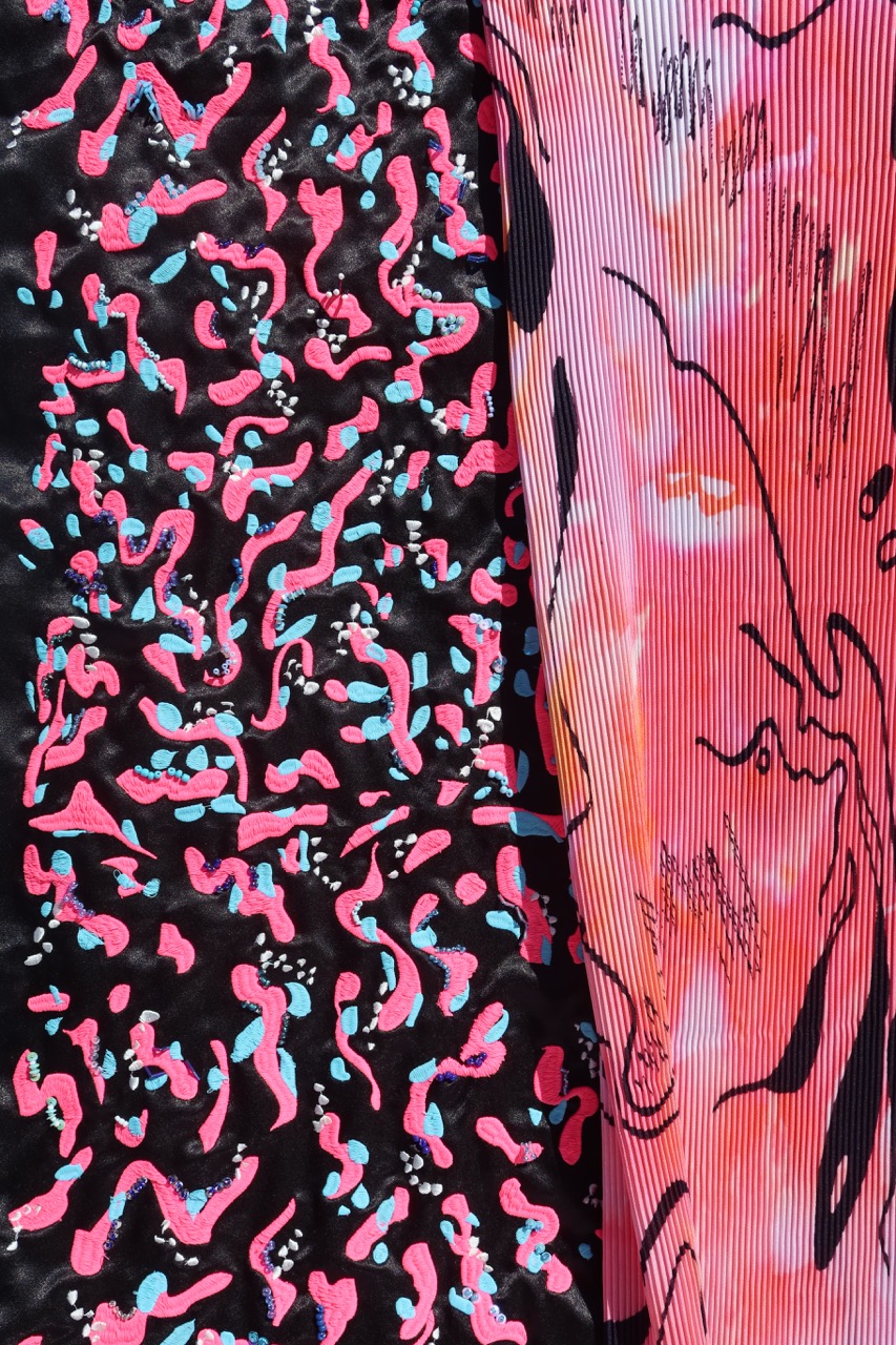 Two fabric swatches side by side: on the left, a pattern of pink and blue abstract shapes on a black background; on the right, a pink and white striped fabric featuring a stylised face design. Both fabrics showcase vibrant colours and unique patterns.