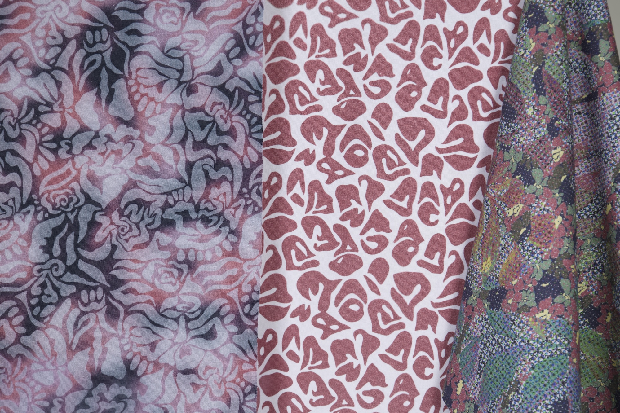 Three pieces of patterned fabric displayed side by side. The left fabric features a floral design in shades of pink and grey, the centre fabric showcases abstract shapes in pink, while the right fabric has a vibrant multicoloured pattern resembling natural textures.