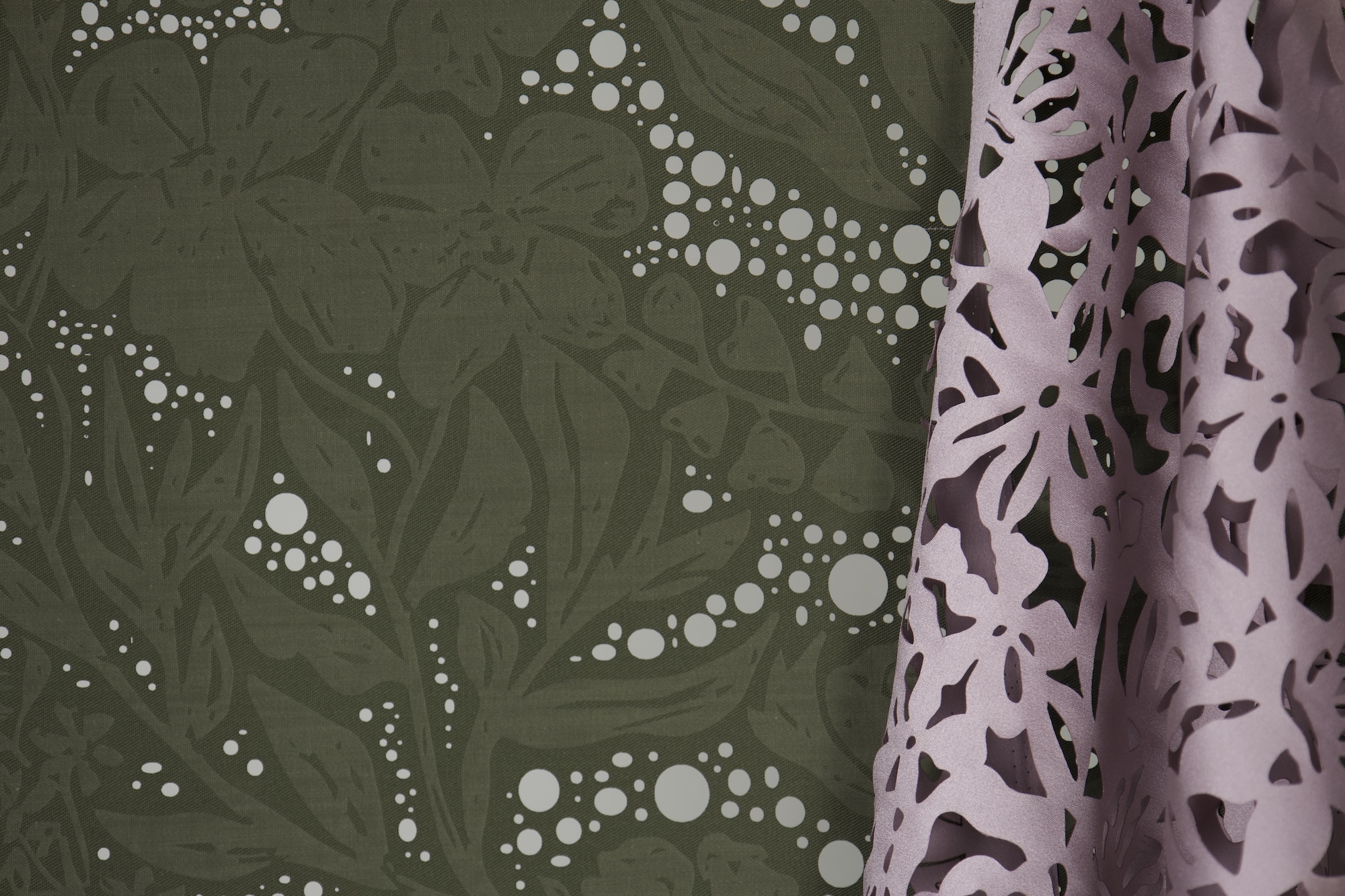 A close-up view of a patterned green fabric featuring white floral and bubble motifs, accompanied by a pink decorative curtain with cut-out floral designs. The contrasting textures and colours are clearly visible.