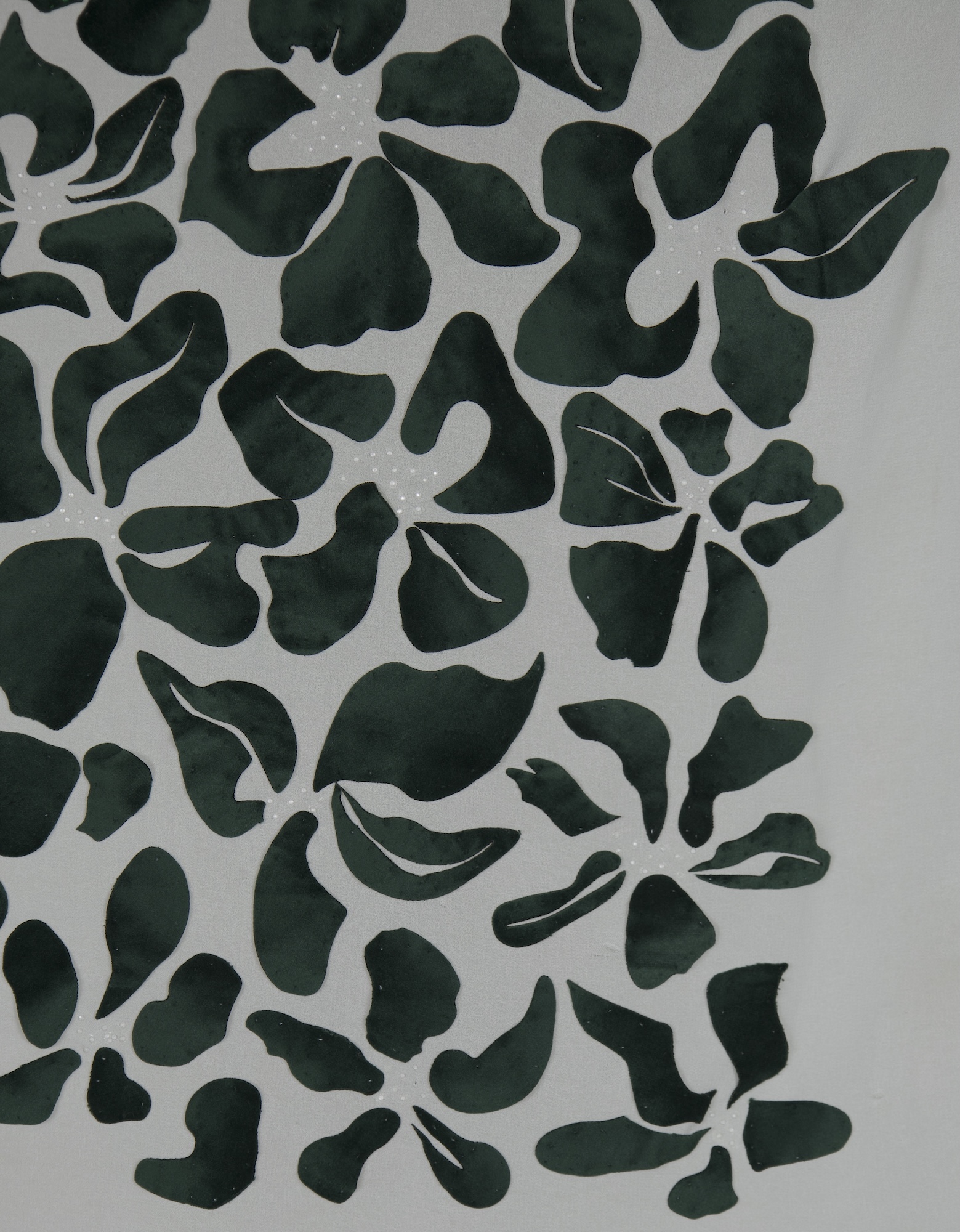 A decorative artwork featuring a pattern of cut-out green leaves on a light grey background. The leaves vary in shape and are arranged densely, creating a layered effect with some negative space visible between them.