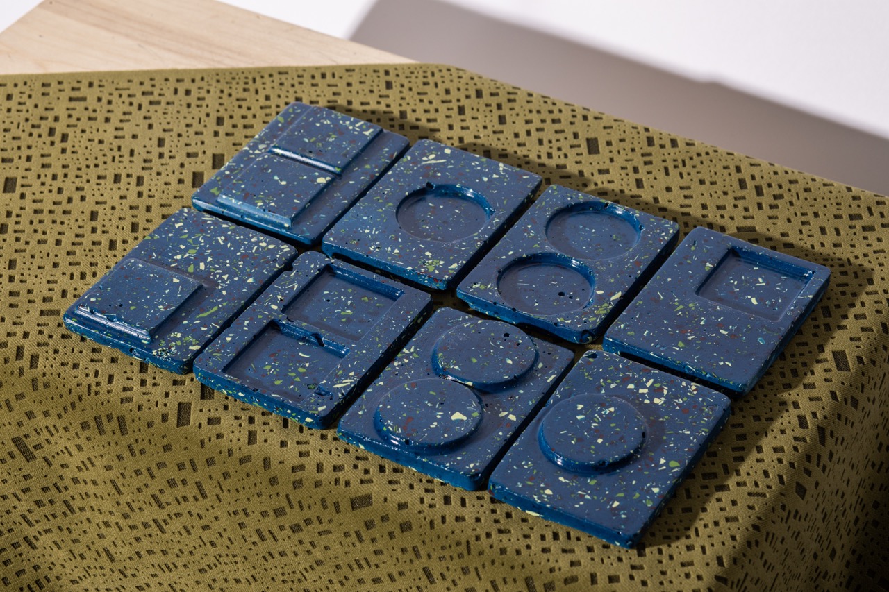 A collection of blue shapes made from a glossy material, featuring various geometric forms such as rectangles and circles, displayed on a textured olive green tablecloth with a patterned design.