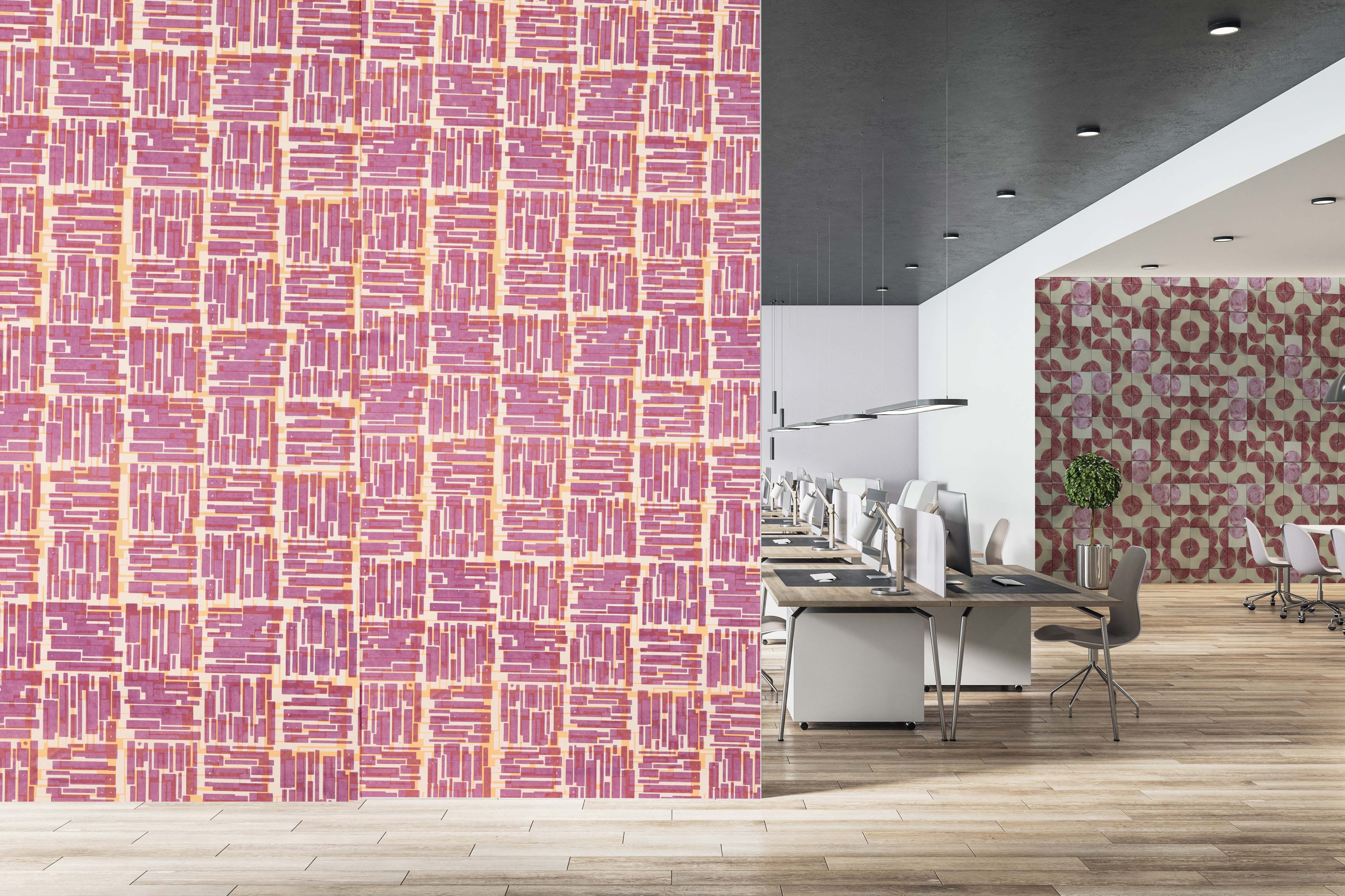 An interior office space featuring a vibrant pink and orange patterned wall on the left, contrasting with a geometric patterned wall on the right. The floor is wooden, and several desks with computers are arranged in the centre of the room.