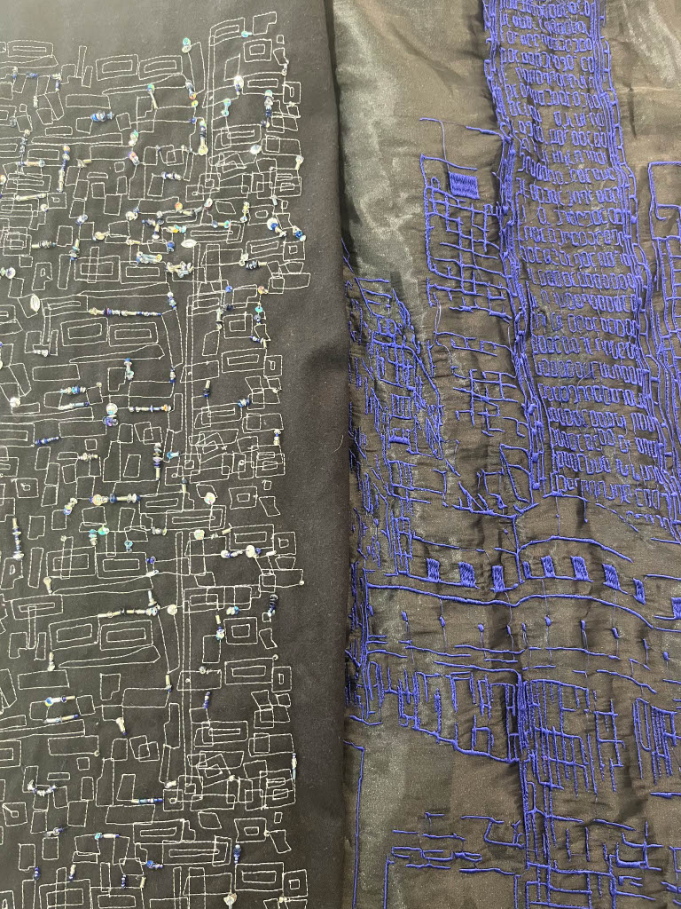 A close-up of two pieces of fabric. The left fabric features intricate white and silver embroidery on a black background, resembling a circuit pattern. The right fabric displays blue embroidery on a black background, depicting a city skyline.