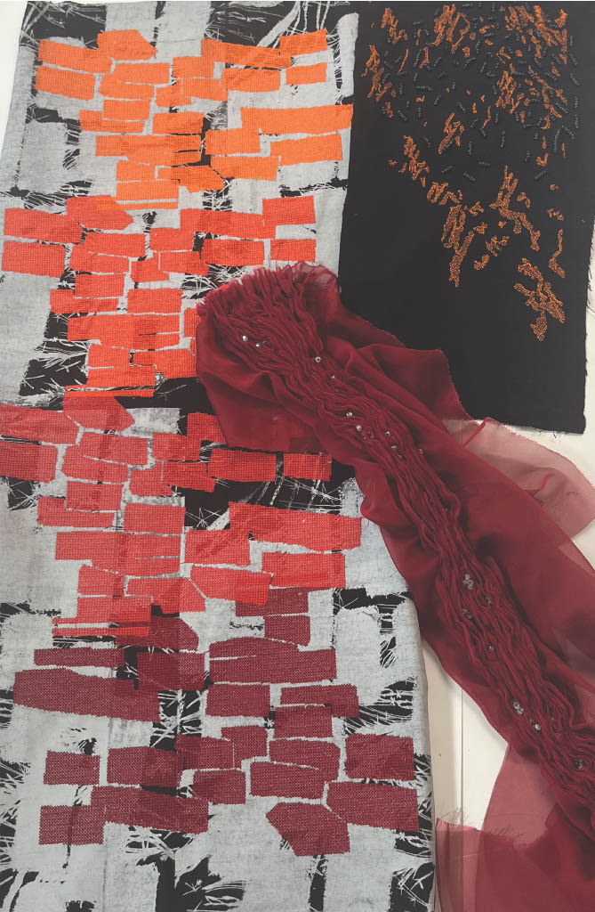 A fabric arrangement featuring a patterned piece with red and orange brick-like designs on a grey background, alongside a solid black piece with textured detail, and a flowing maroon scarf draped on top.