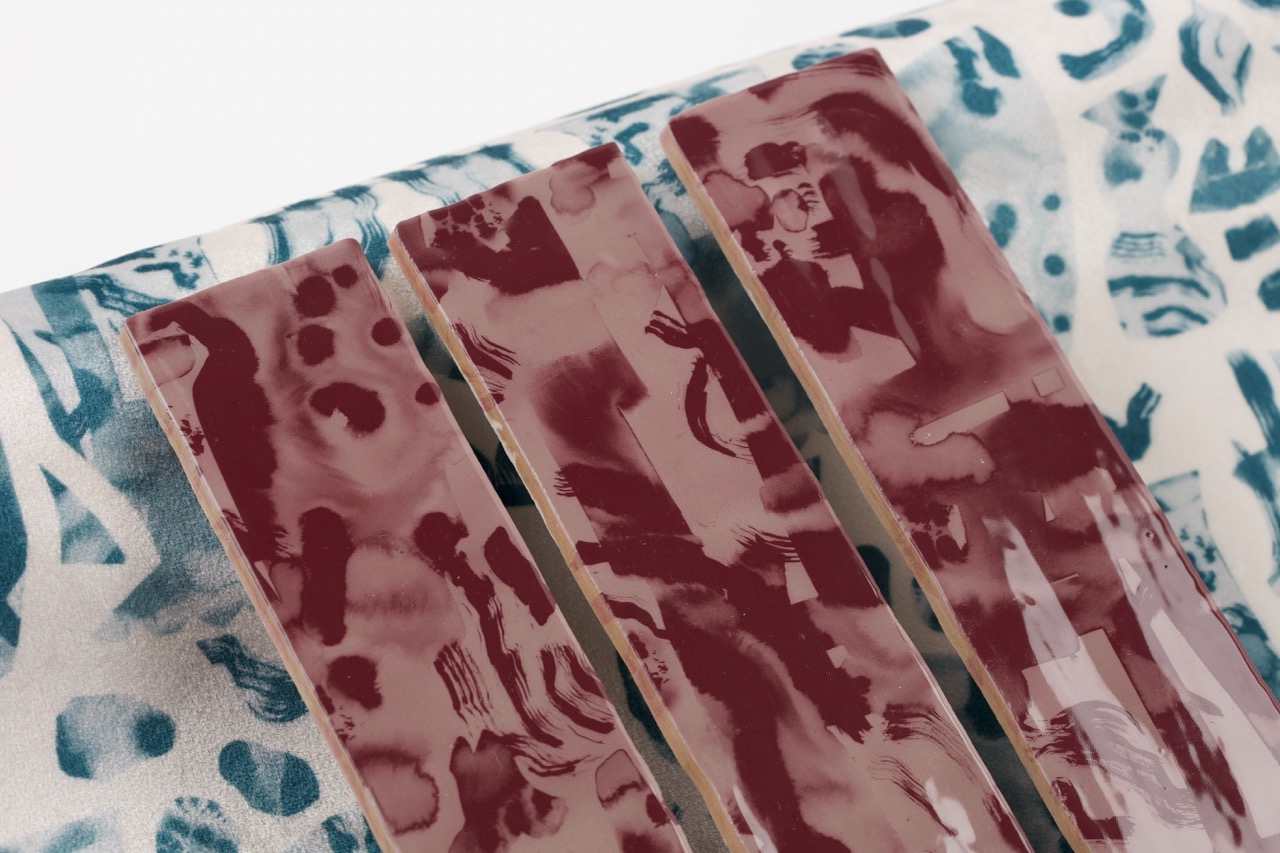 Three rectangular panels with a maroon and white abstract design are positioned on a patterned fabric. The fabric features a blue and white design, with various shapes and textures visible in the background.