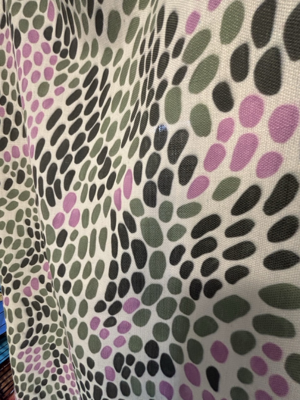 A patterned fabric featuring a design of varying sizes of green, grey, black, and pink oval shapes arranged in a repetitive manner. The shapes are primarily in clusters, creating a visually dynamic texture.