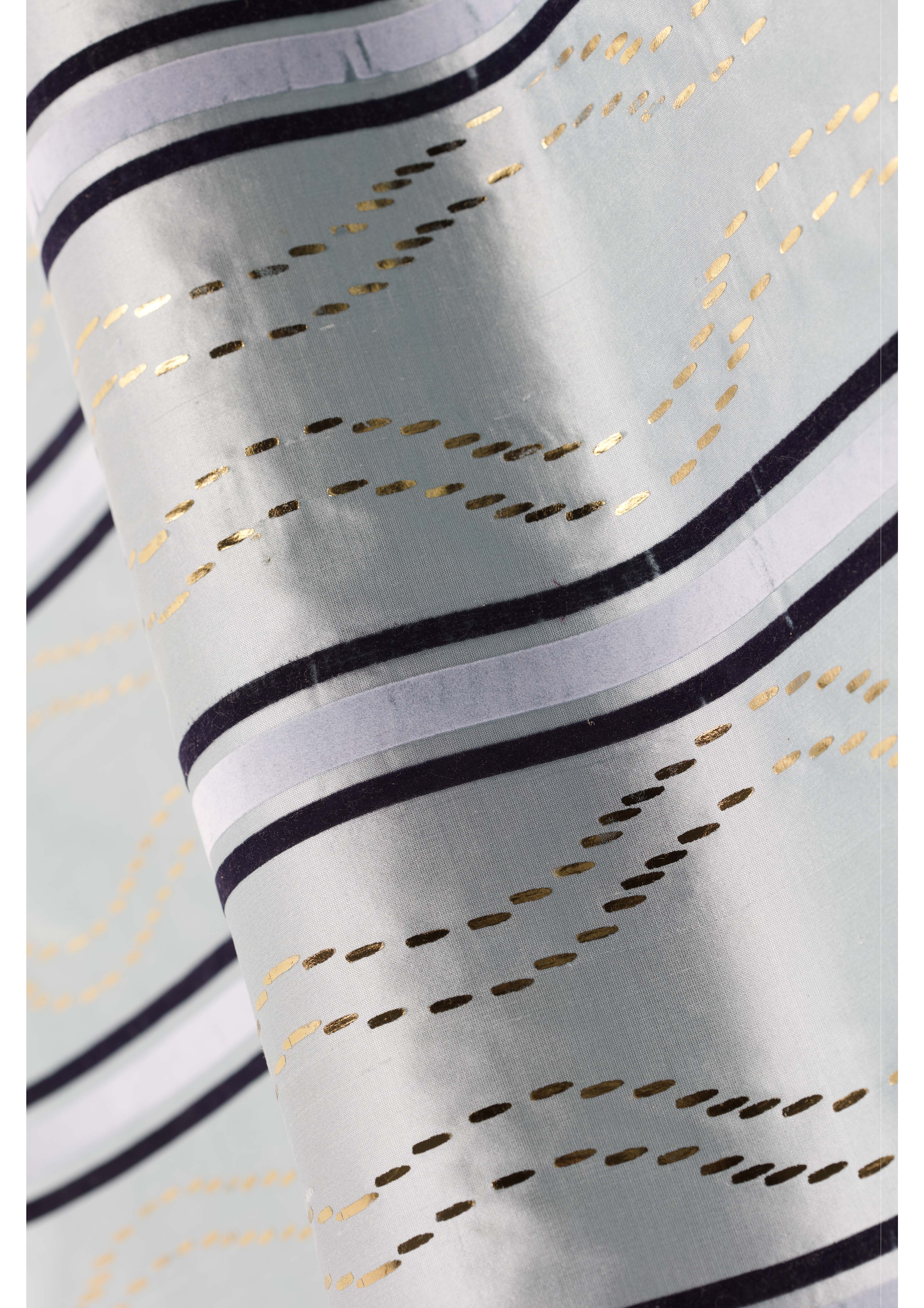 A close-up of a light blue fabric featuring wavy stripes in gold, black, and white. The fabric has a glossy texture, with intricate patterns created by alternating lines and dotted motifs.