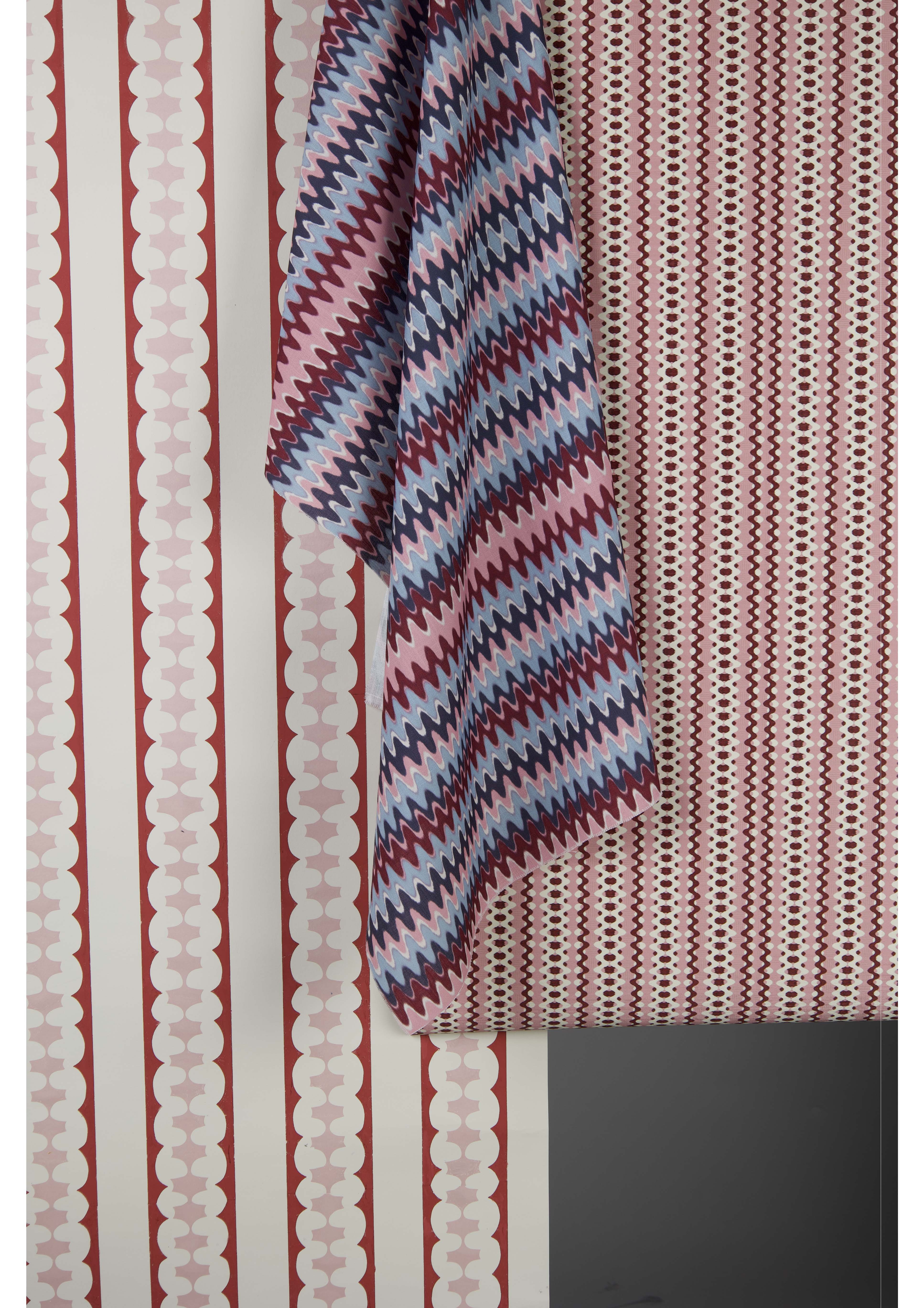A close-up of two wallpaper patterns. One features vertical stripes in red and white with circular motifs, while the other is a zigzag design in shades of purple, blue, and maroon, hanging over the edge.