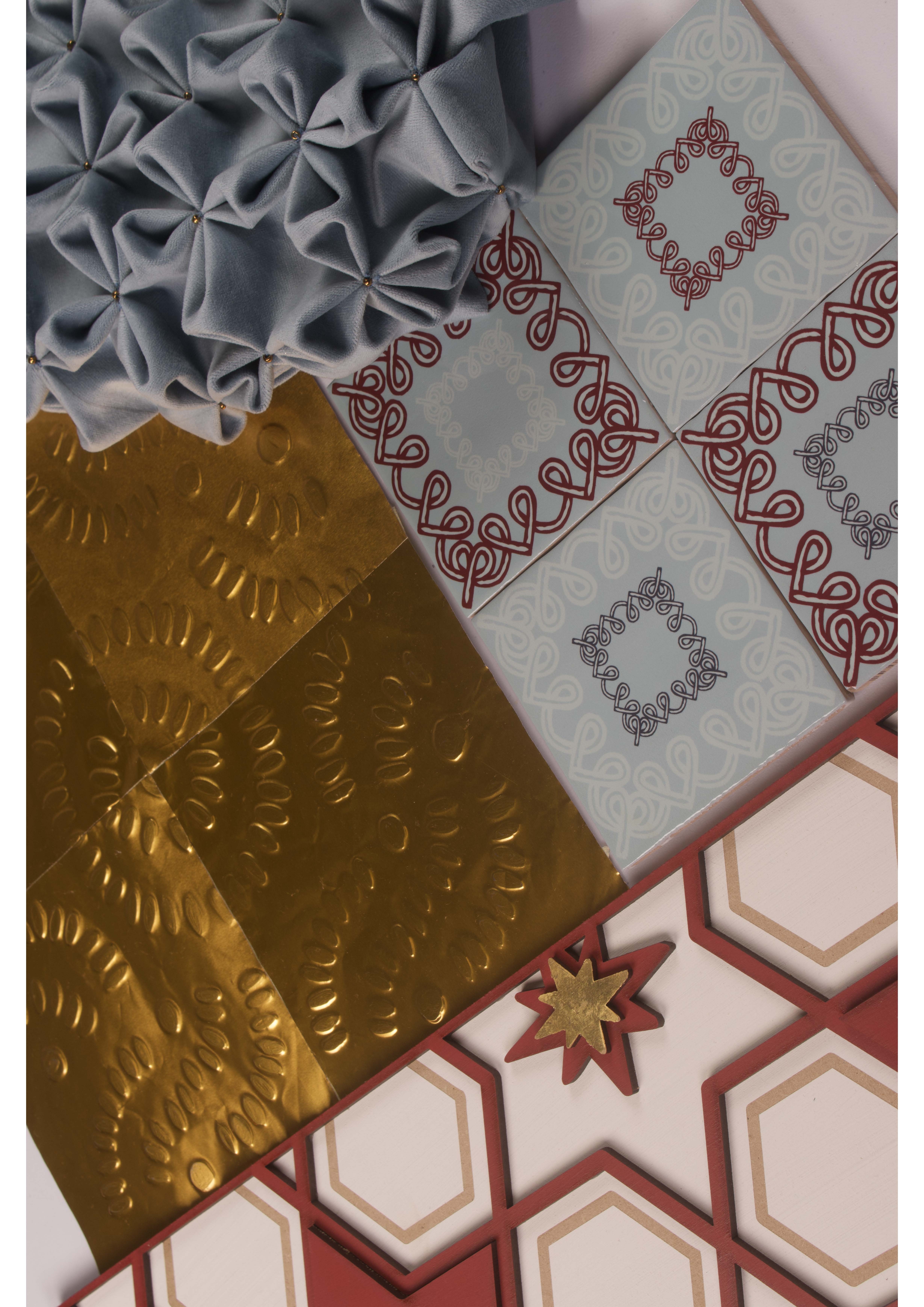 An assortment of decorative tiles laid out in a flat arrangement. The collection includes patterned tiles in shades of blue, gold, and red, with intricate designs and a textured fabric piece in grey, creating a varied visual display.