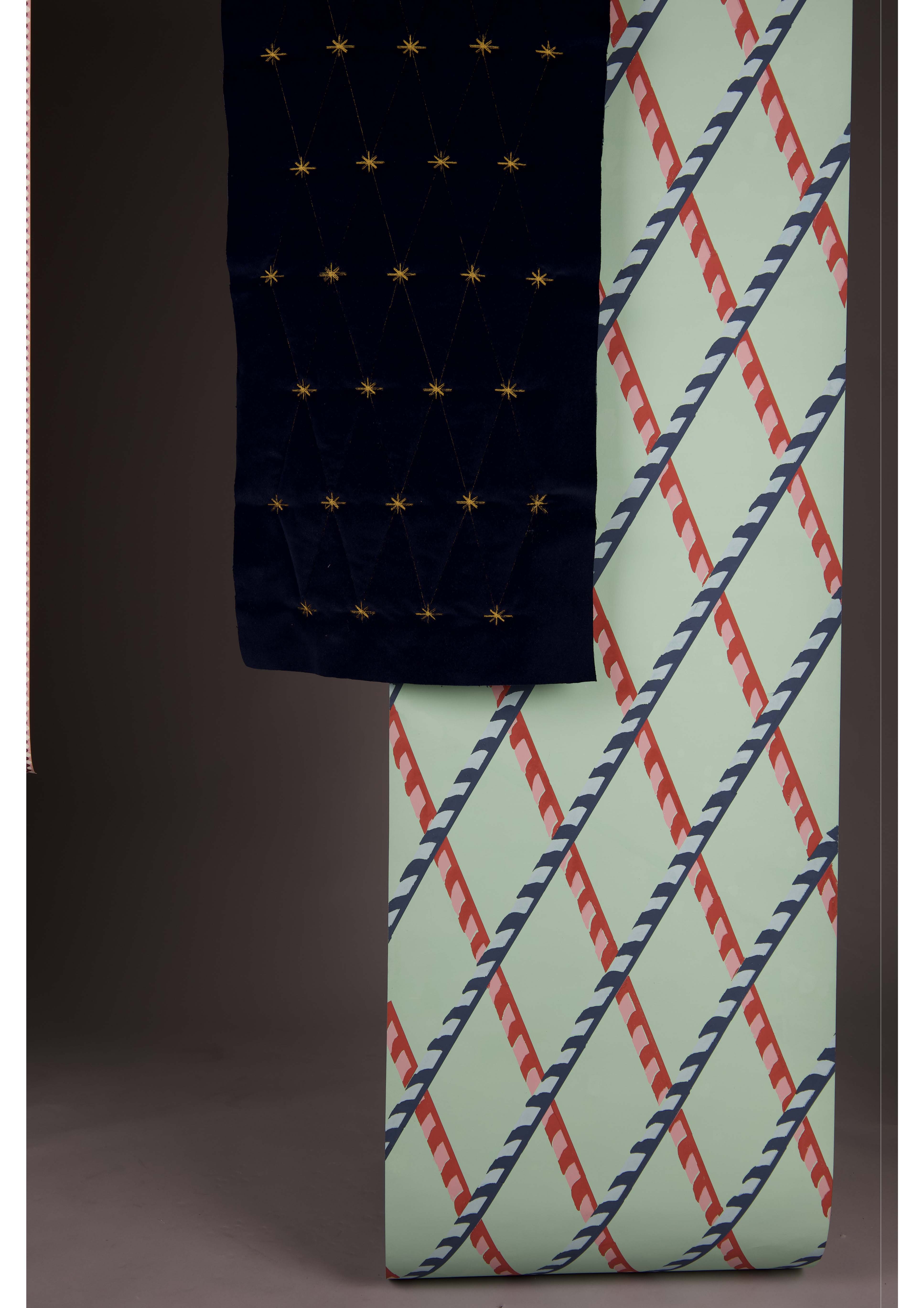 A folded navy blanket with gold star patterns hangs beside a patterned fabric featuring diagonal lines in red, blue, and green. The background is dark, highlighting the colourful designs.