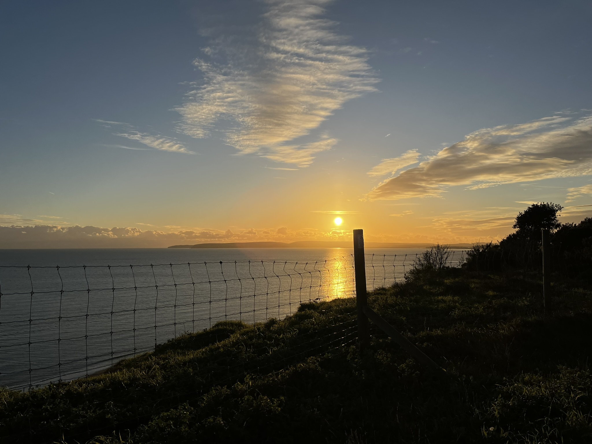 The sea and Studland Bay viewed from a clifftop in Bournemouth, with the sun setting above it
