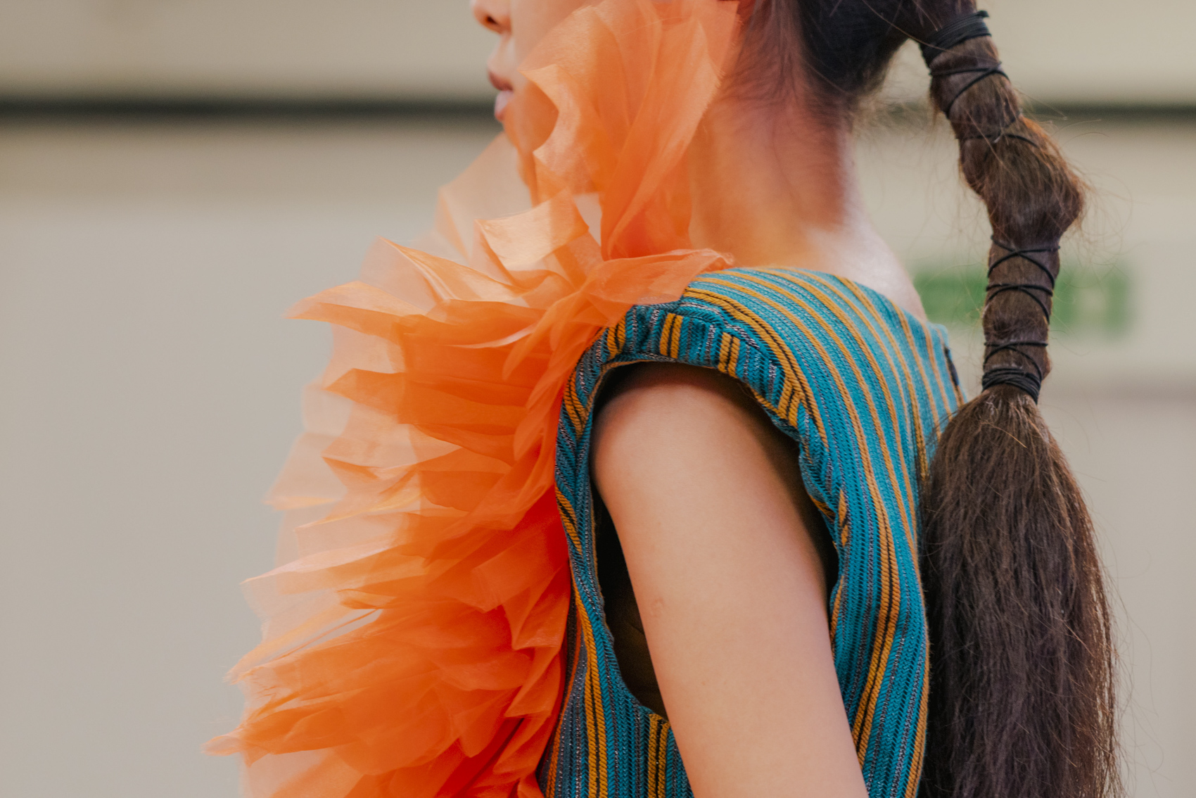Model wearing turquoise garment and orange piece, close-up side profile.