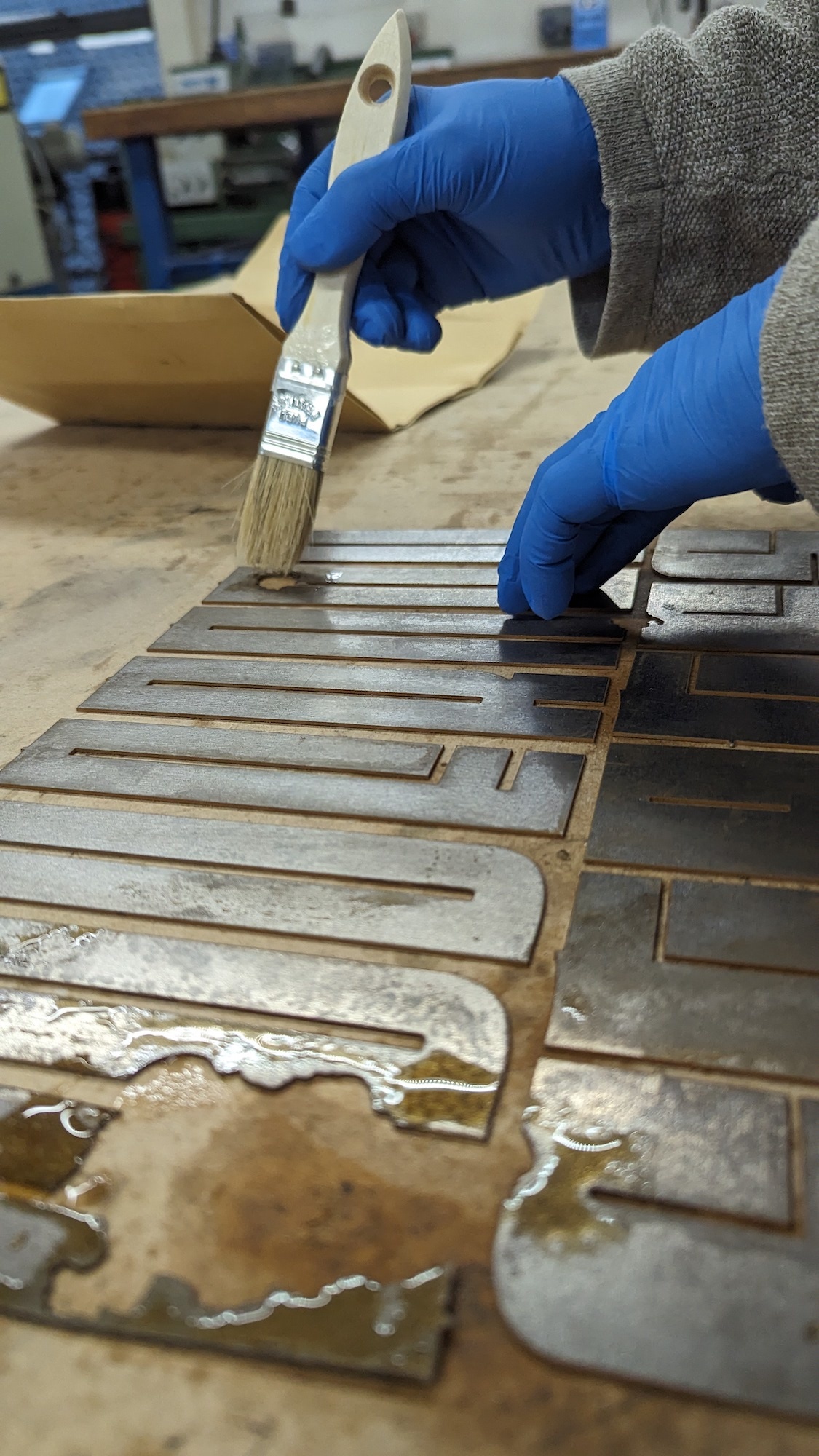 A student wearing blue gloves applies a chemical to some metal letter press plates.