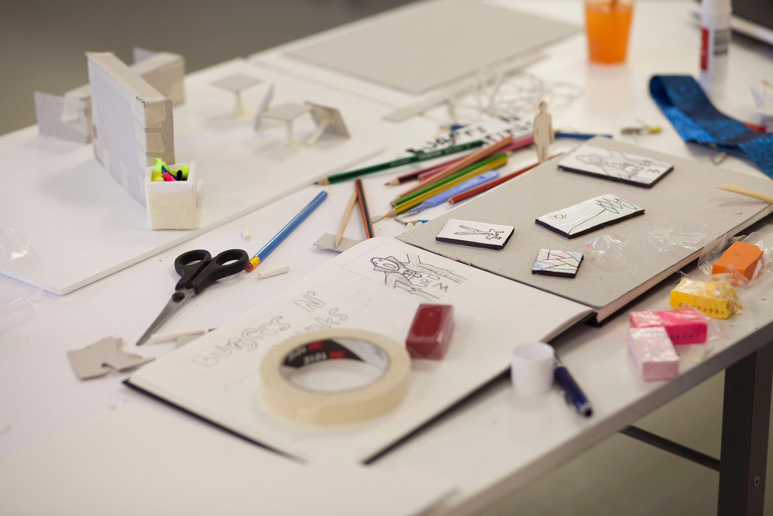 Close-up of a student's work book, pencils, scissors and tape are placed around the workspace.