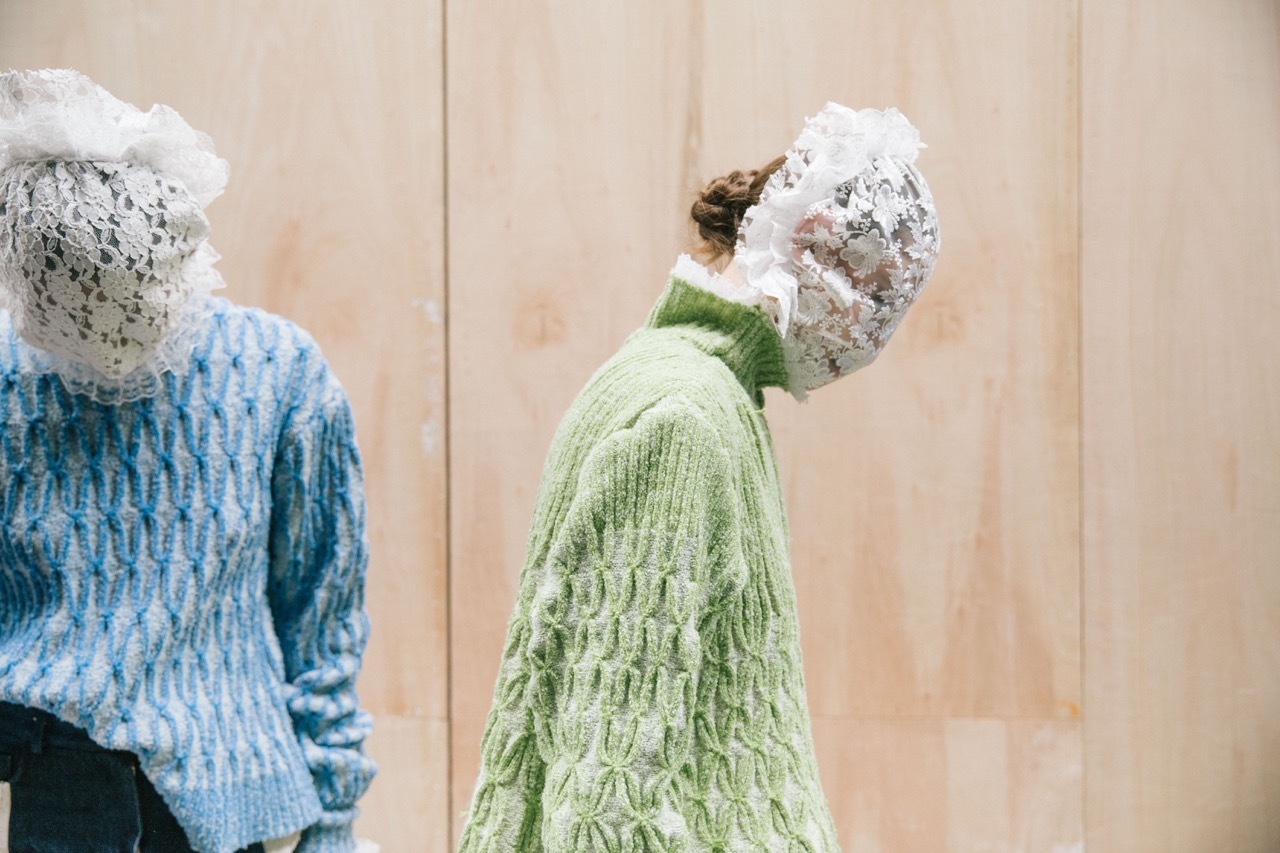 Two masked models wearing green and blue sweaters.