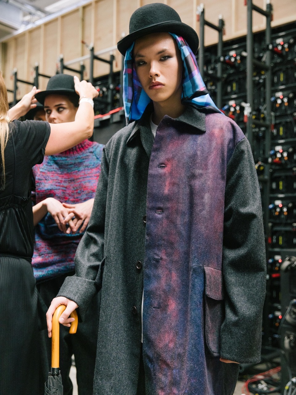 A model a black pink-dyed coat with a top hat, headpiece and cane.