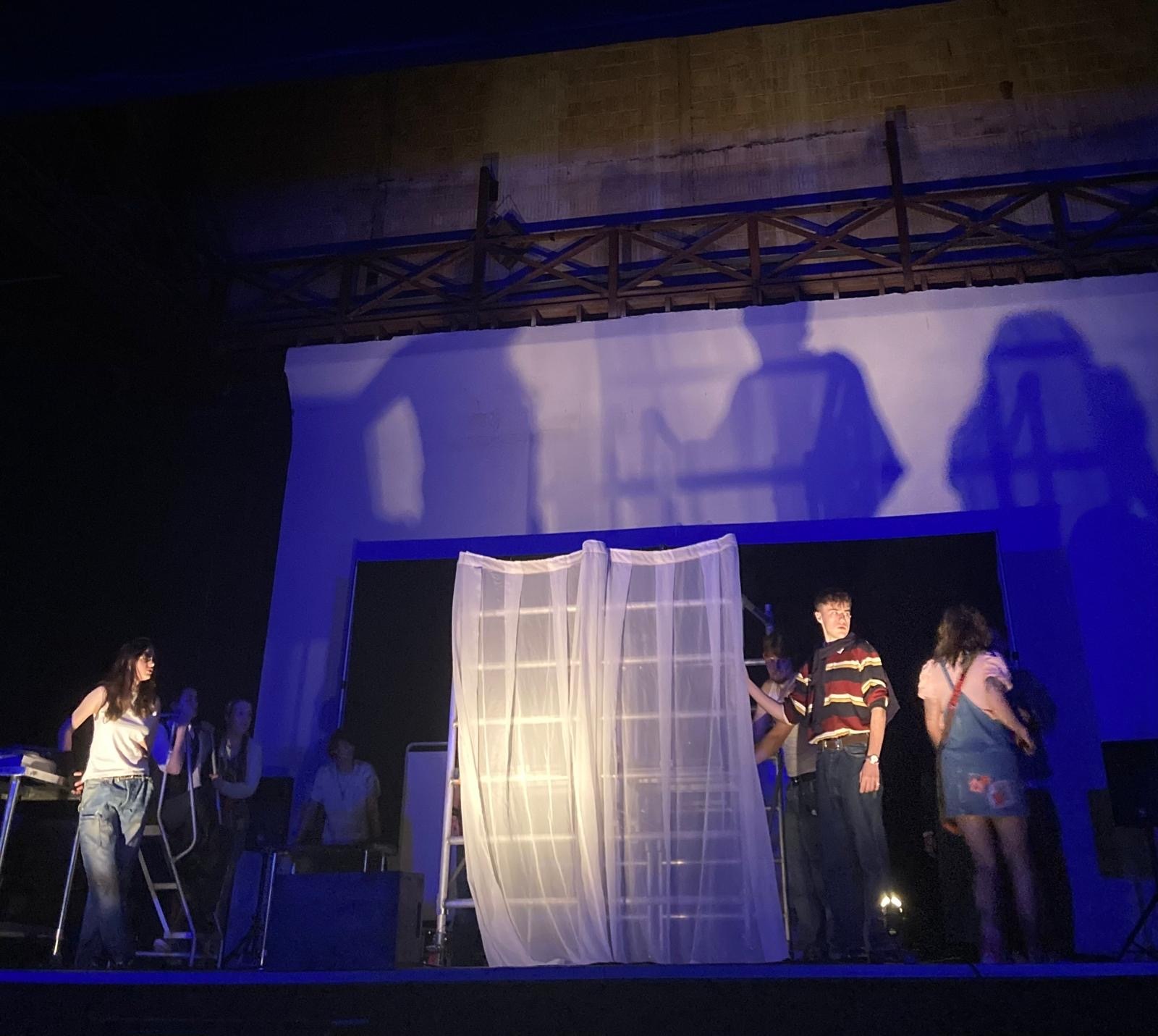 Actors on stage under blue light performing.