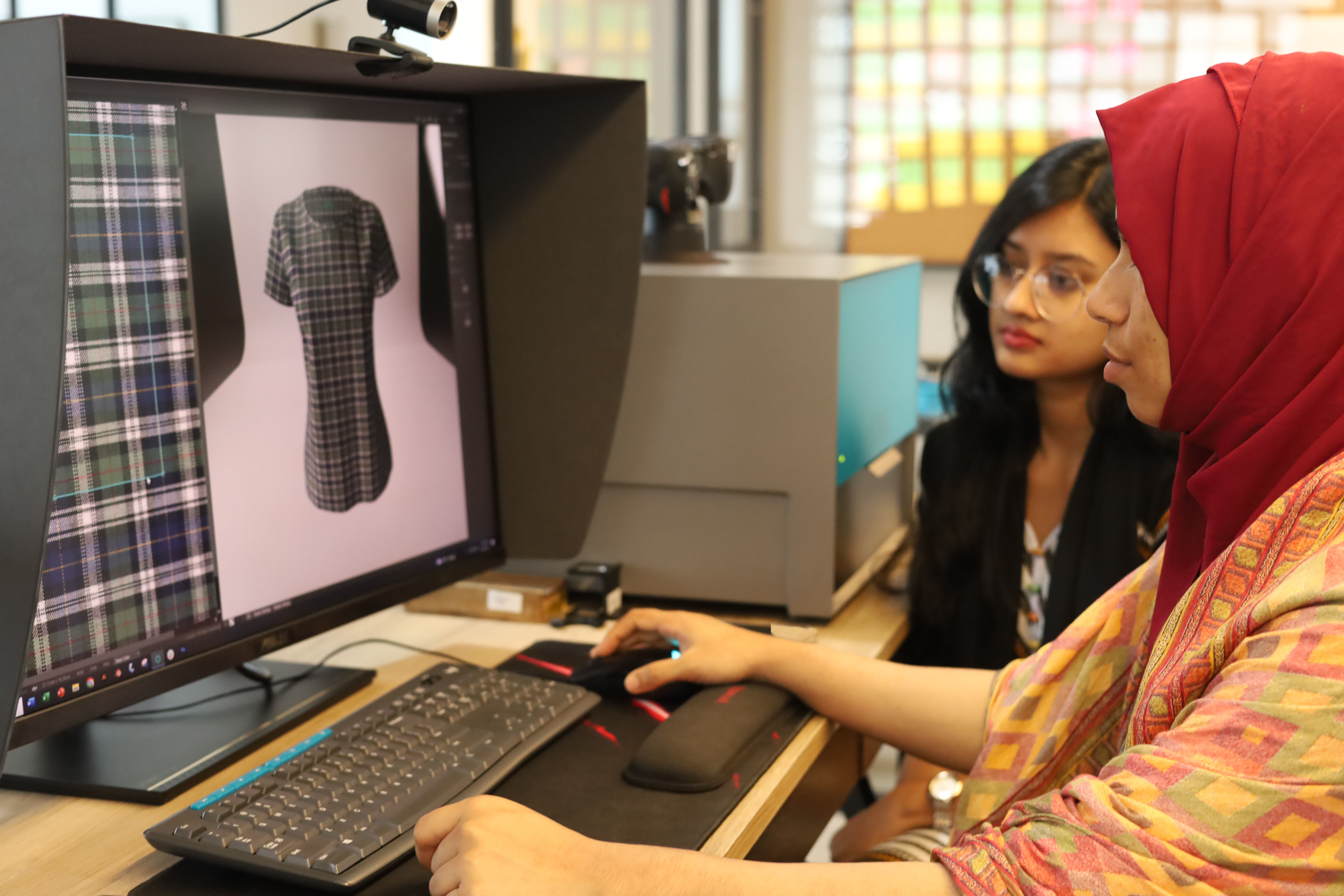 Two people using digital fashion software on a computer, with a digital fabric and garment on the screen.