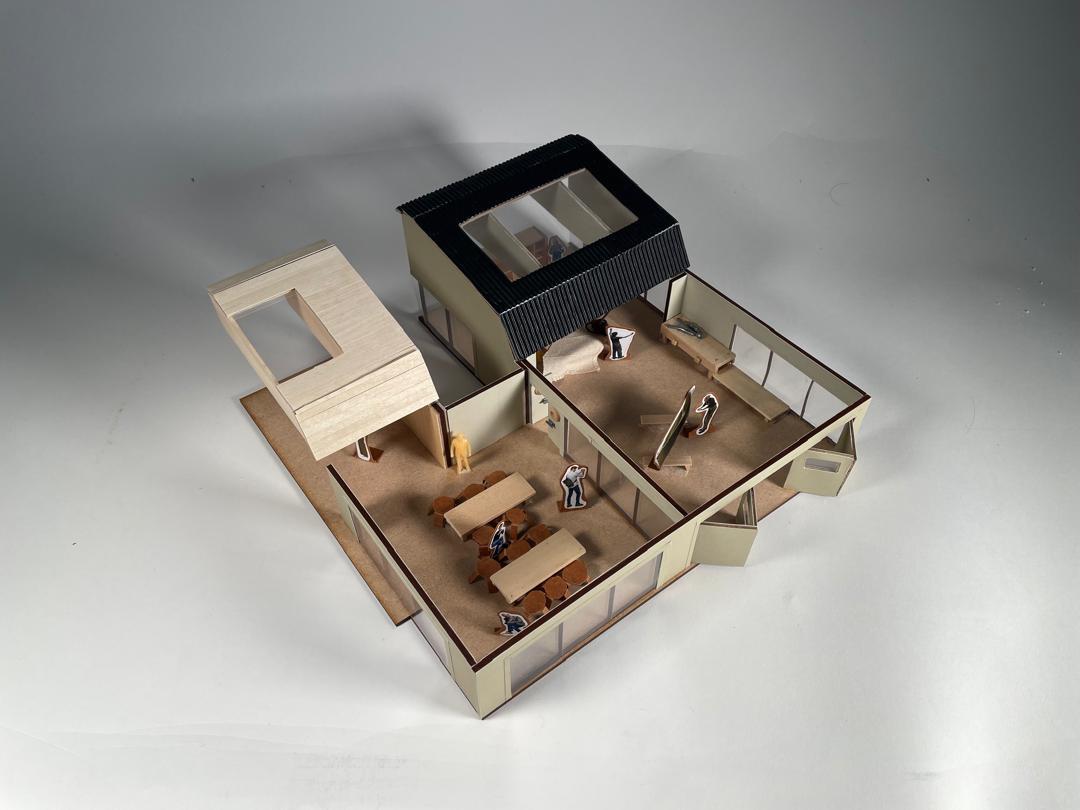 Architectural model with cutaway view showing interior rooms, beige and black exterior walls, miniature furniture inside compartments.