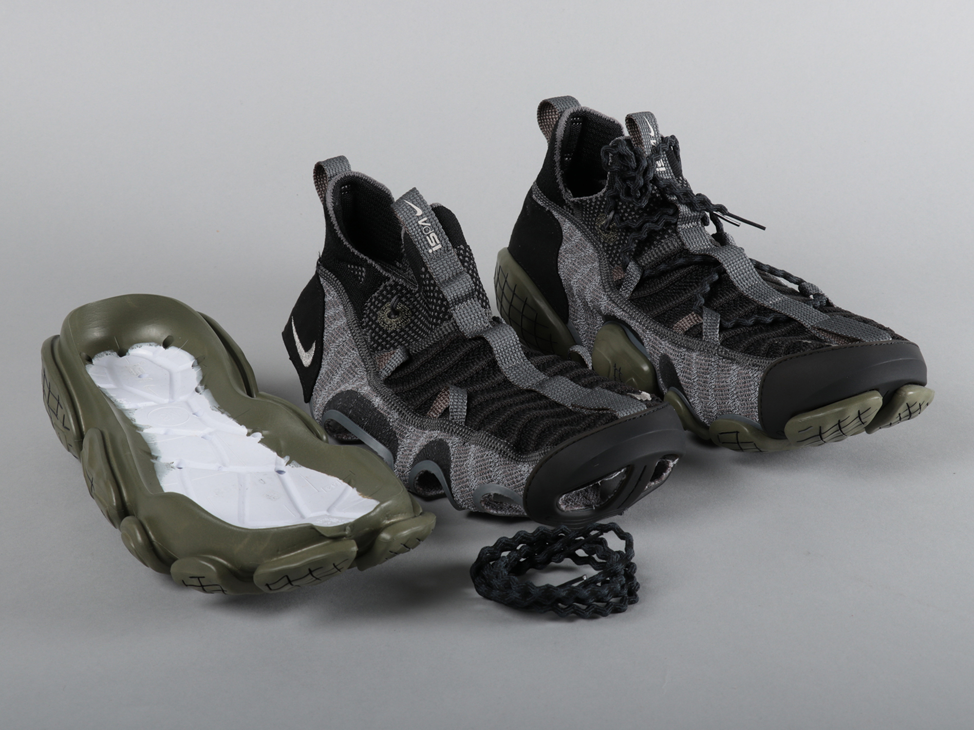 A pair of trainers, one of which has its plastic outer sole removed and placed next to it.