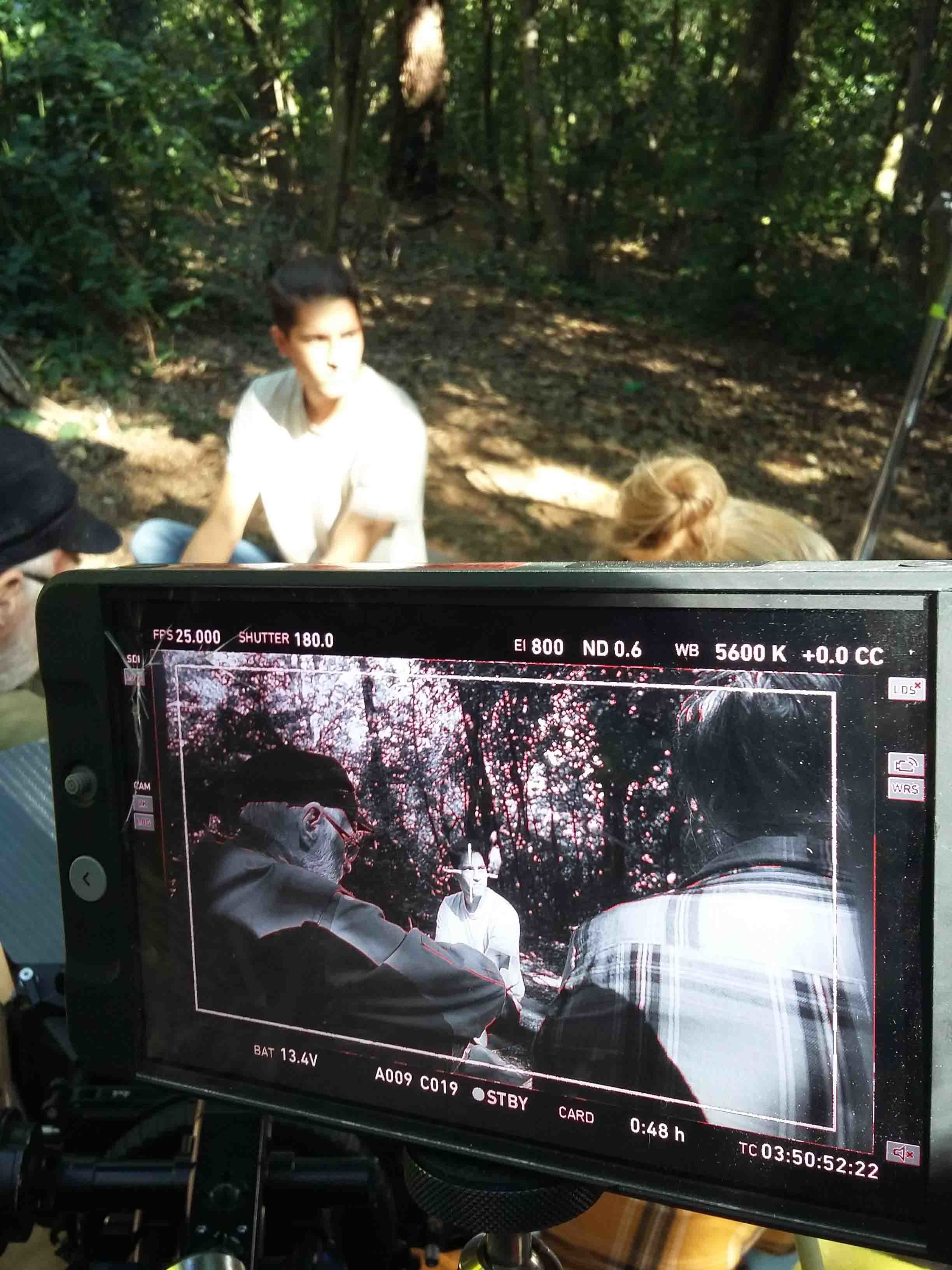 Close-up of a camera monitor while a movie scene is being filmed. Three men are being filmed, two have their backs to the camera.