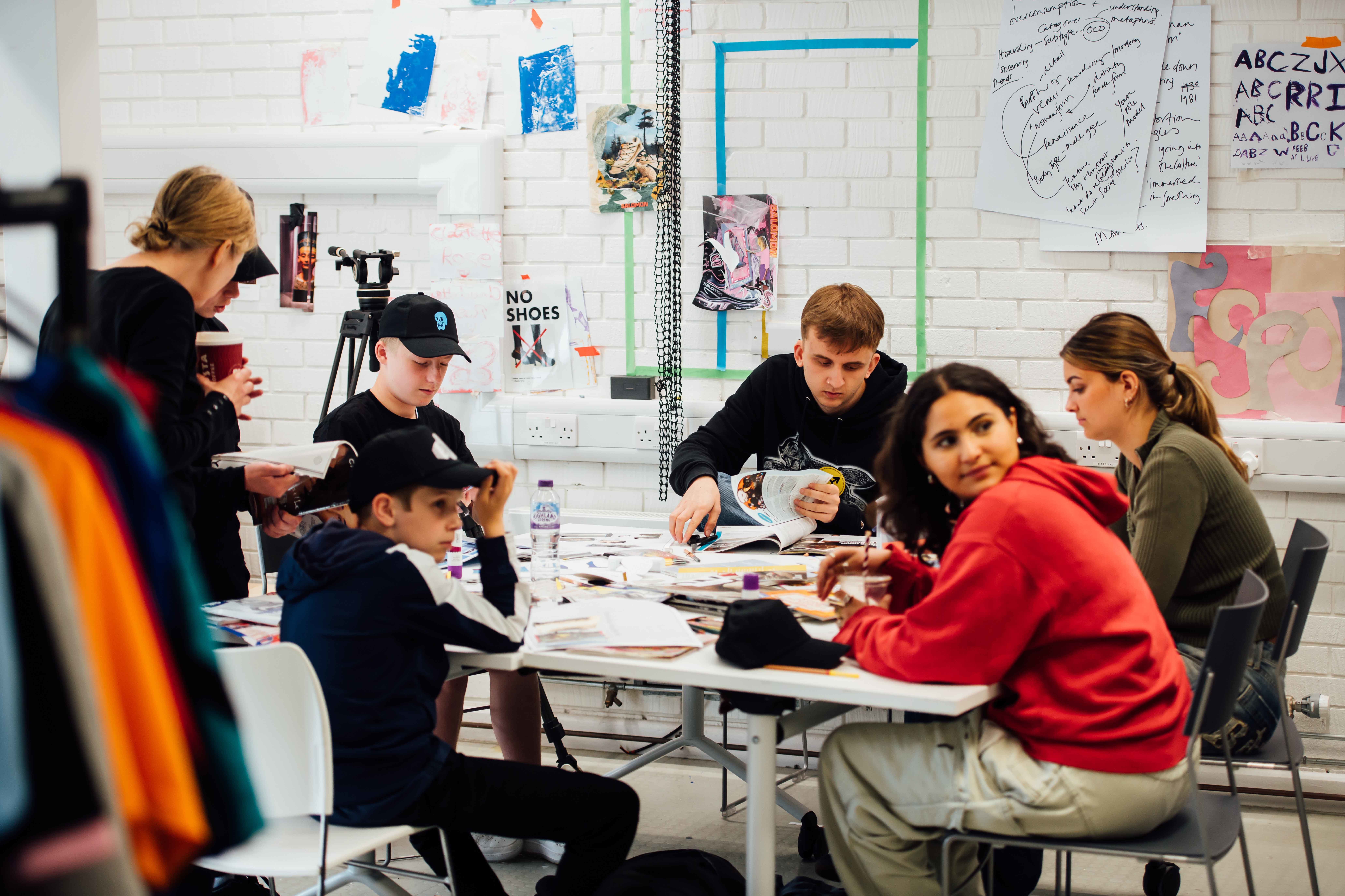 A group of seven students and staff in a colourful studio, sat working on collages.