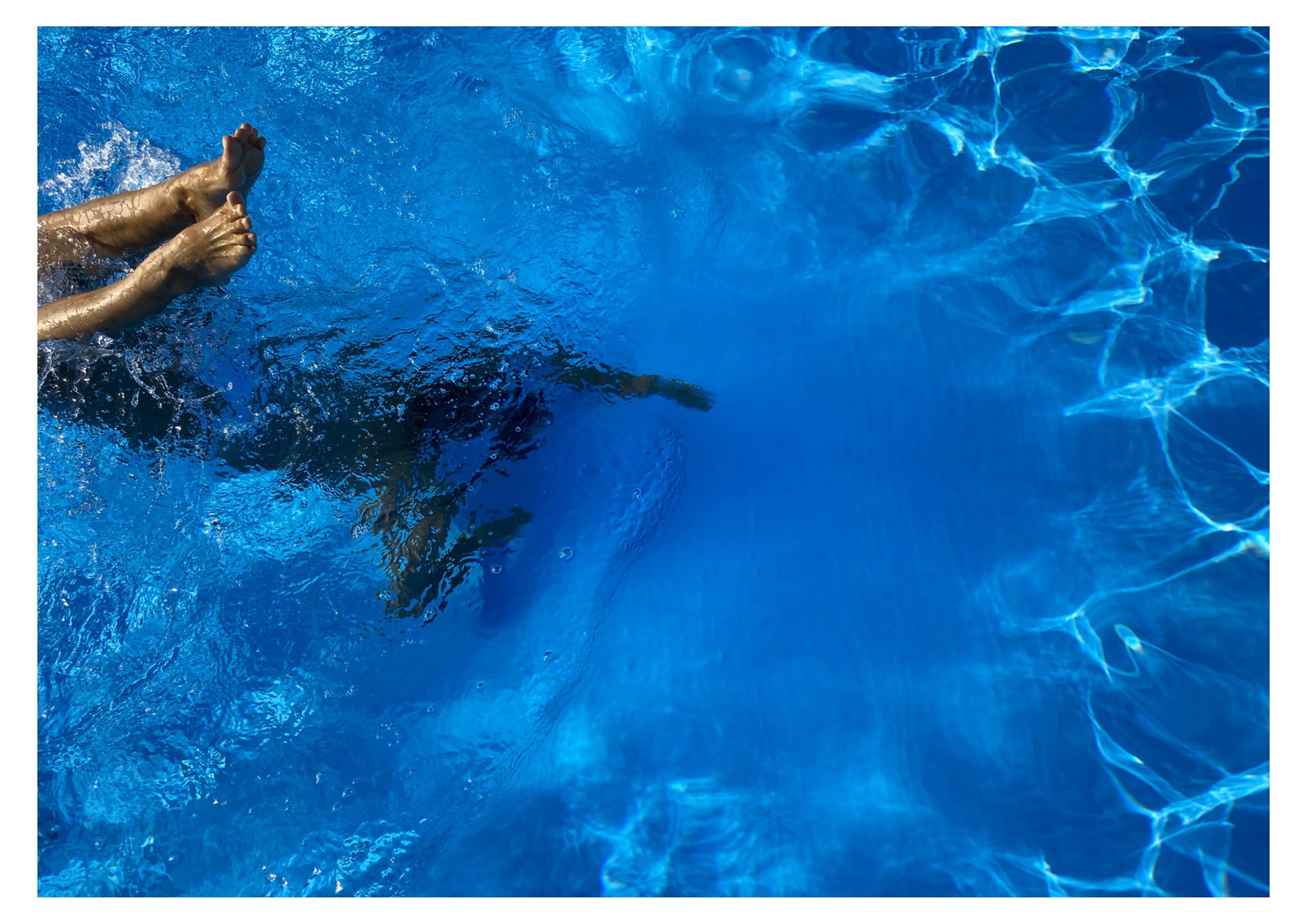 Feet poking out of the water of a swimming pool as if someone has just jumped in