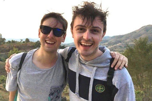 AUB Film Production graduate Ben Harrison with friend Graham Roberts in Thailand. They are pictured smiling at the camera with their arms around each other and a green landscape in the background.