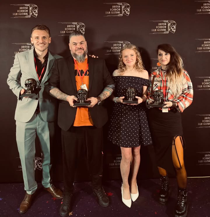 Four people holding trophy statuettes stand in front of a British Horror Film Festival step-and-repeat backdrop.