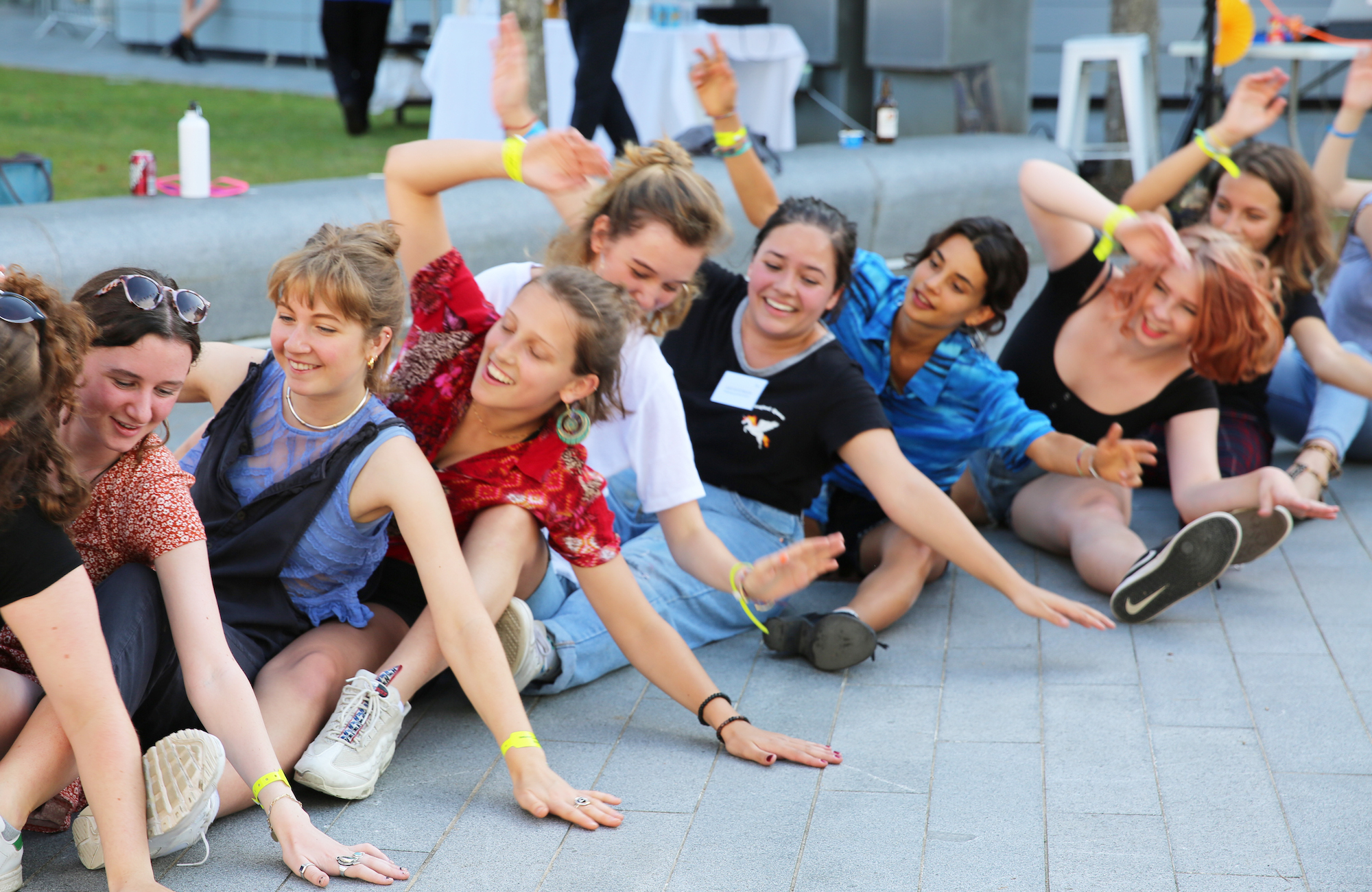 A group of students sitting in a line on the ground on AUB campus and dancing.