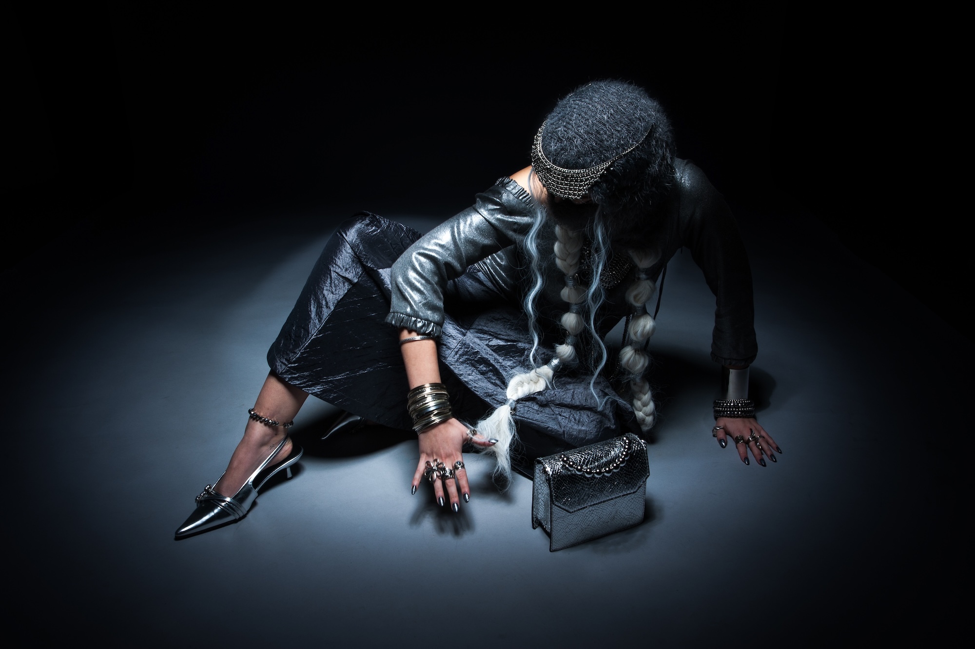 Person in dark clothing crouched on floor. Dark background with spotlight effect.