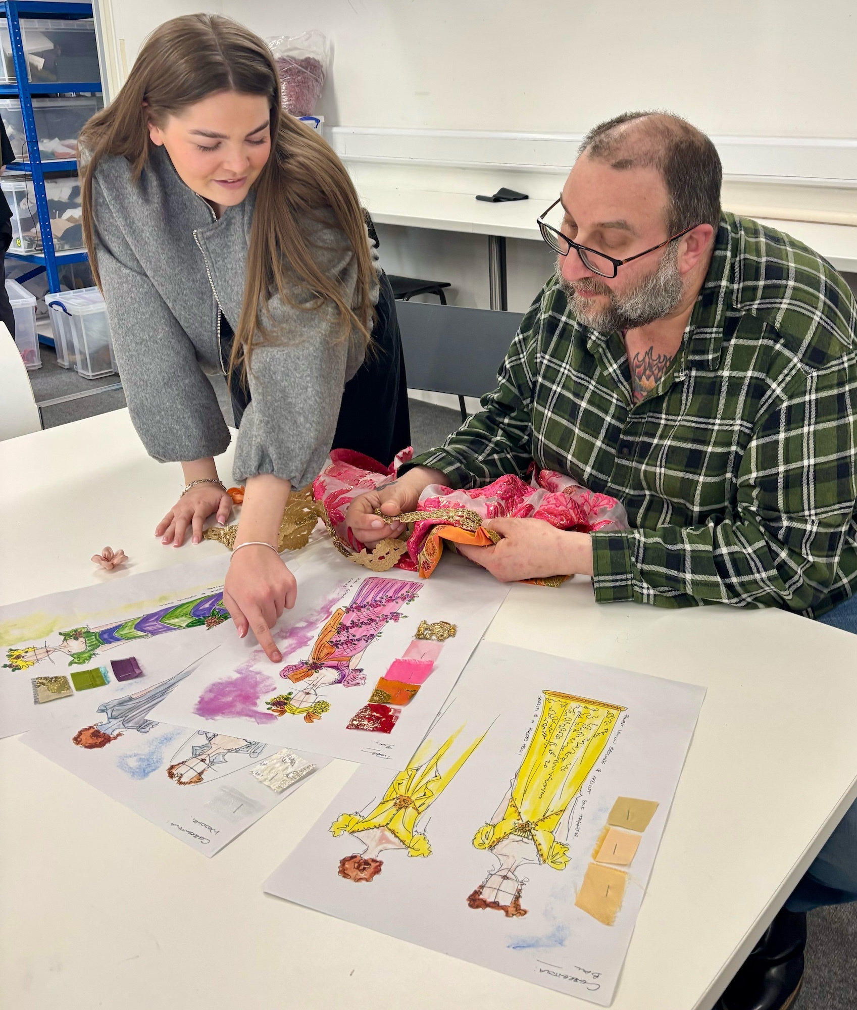 A BA (Hons) Costume student confers with W Martin over colourful costume design illustrations and fabric samples.
