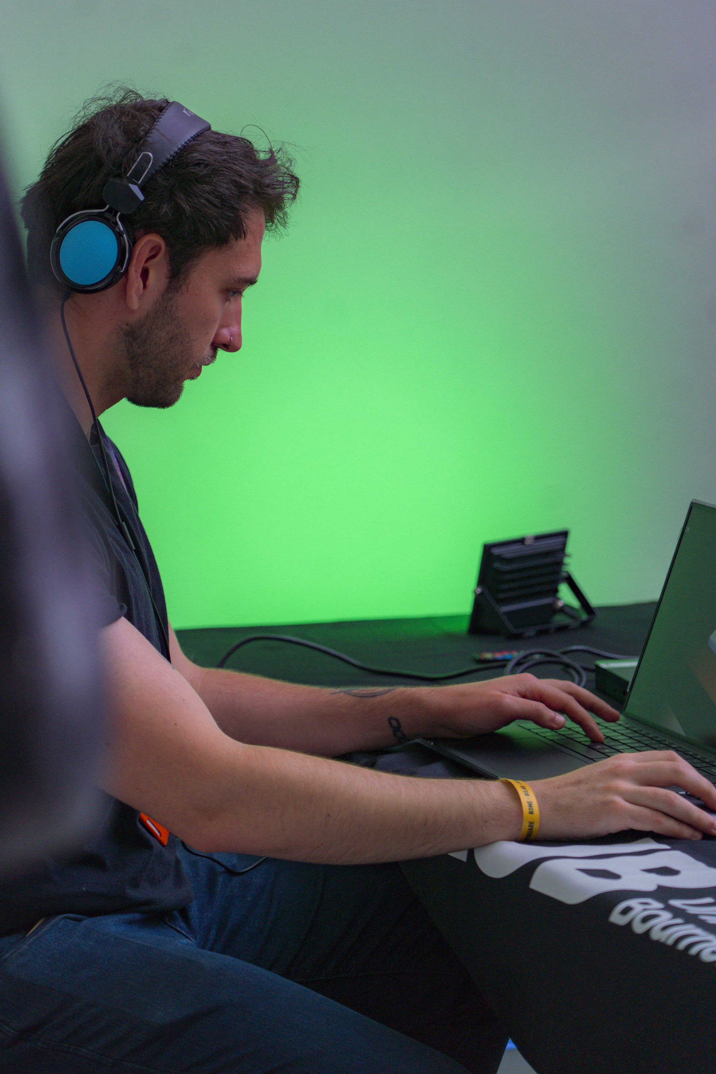 Student interacting with laptop wearing blue headphones, green lighting in the background.
