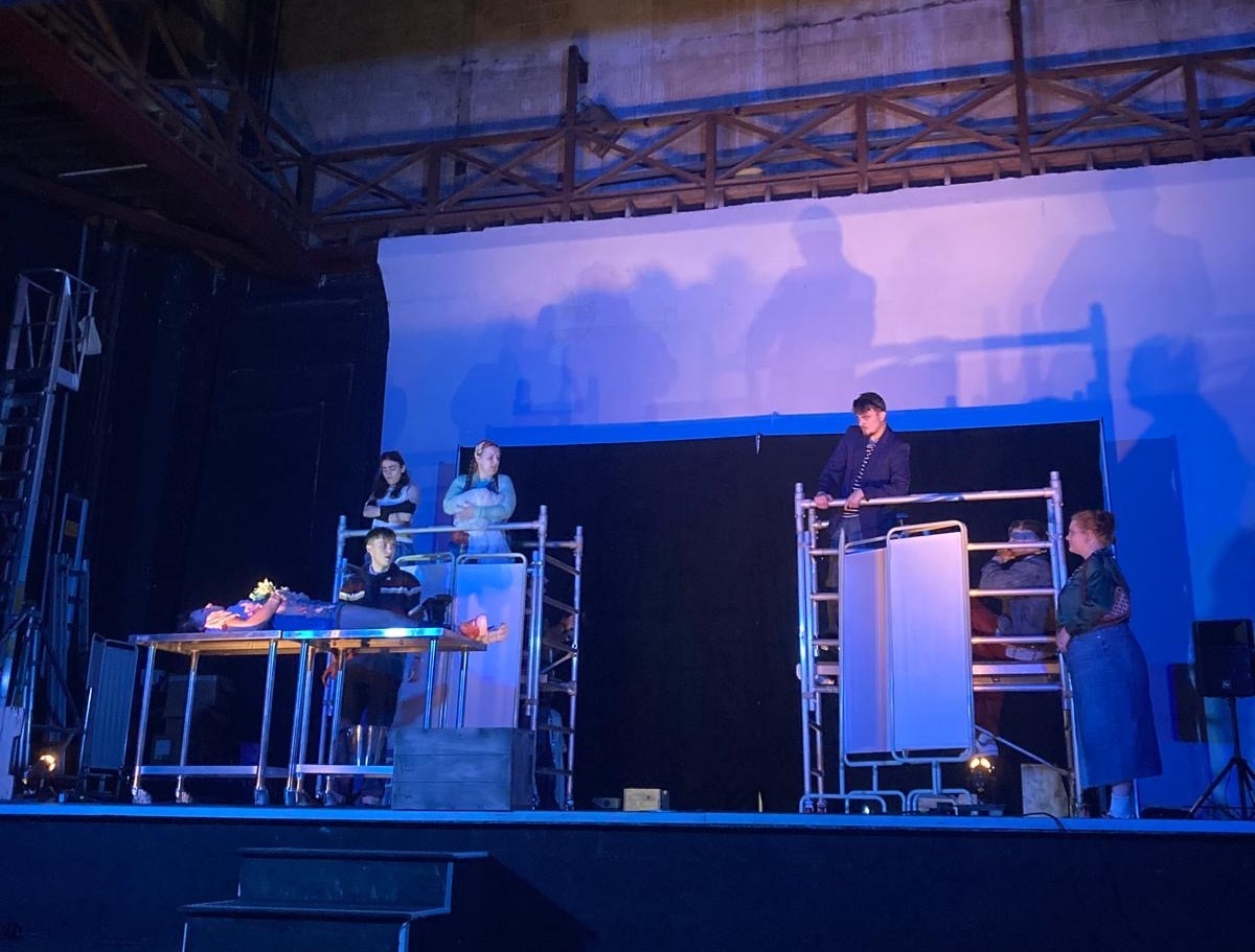 Actors on stage under blue light performing.